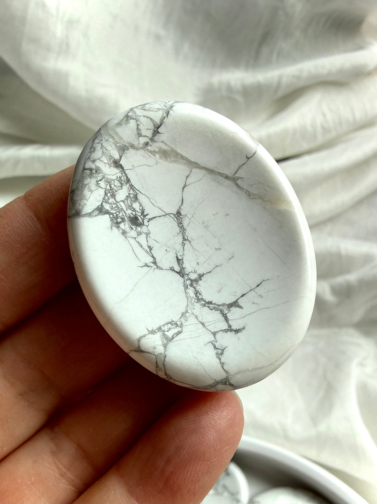 Howlite worry stone held in hand showing intricate gray veining and smooth polished thumb indentation