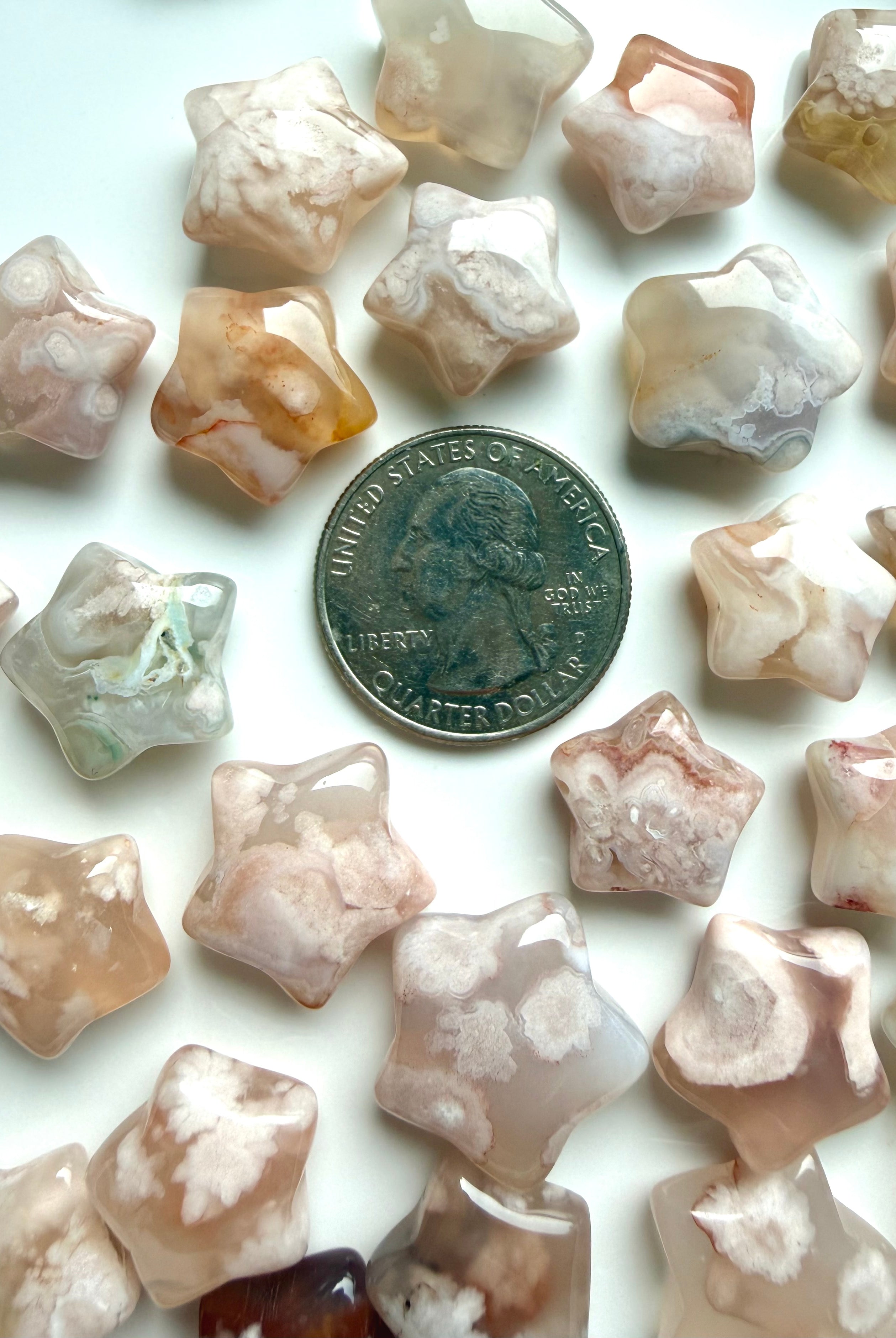 Flower Agate star carvings shown with a US quarter for scale, with creamy pink, peach, and taupe natural inclusions