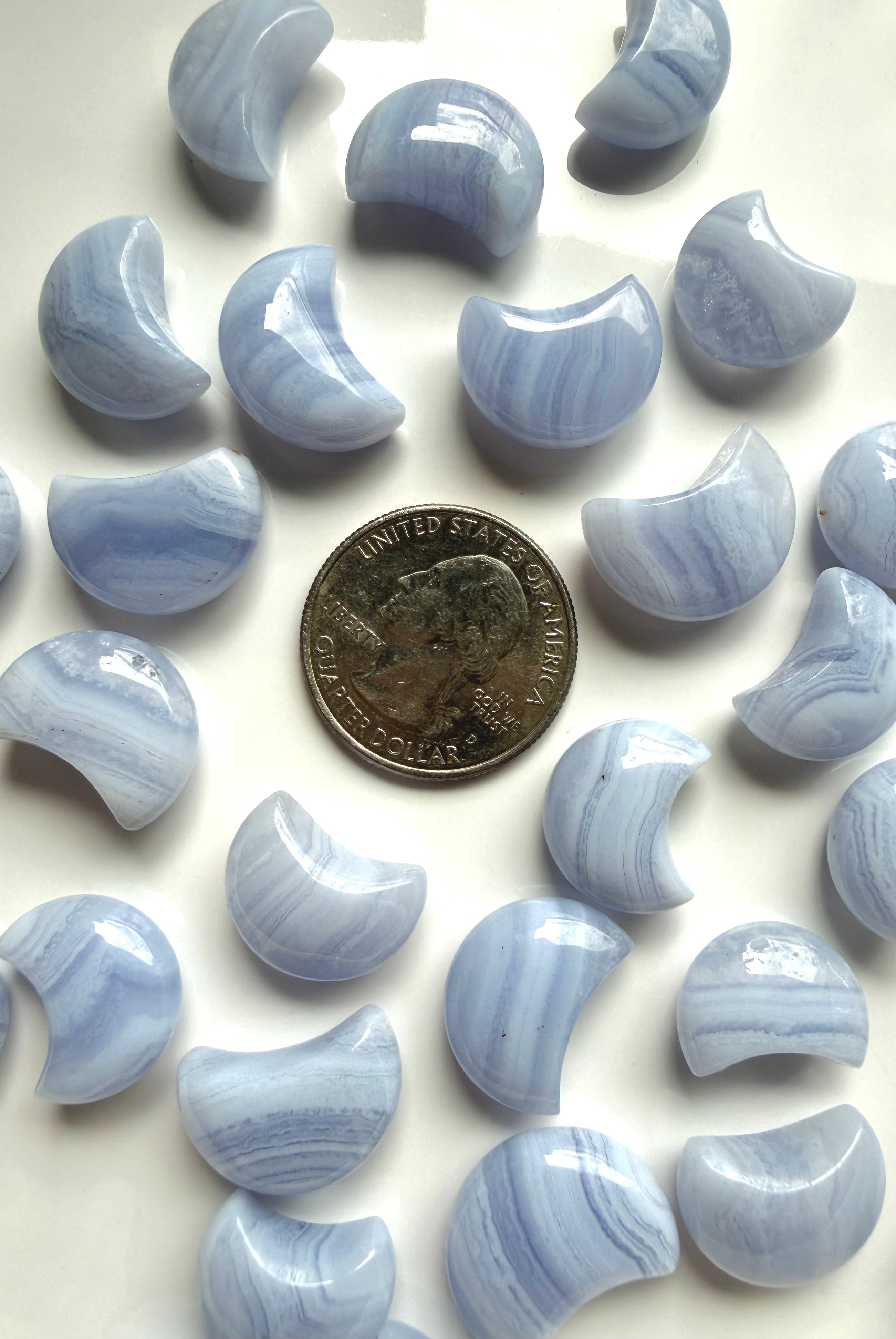 Blue Lace Agate crescent moon carvings beside a U.S. quarter for size comparison
