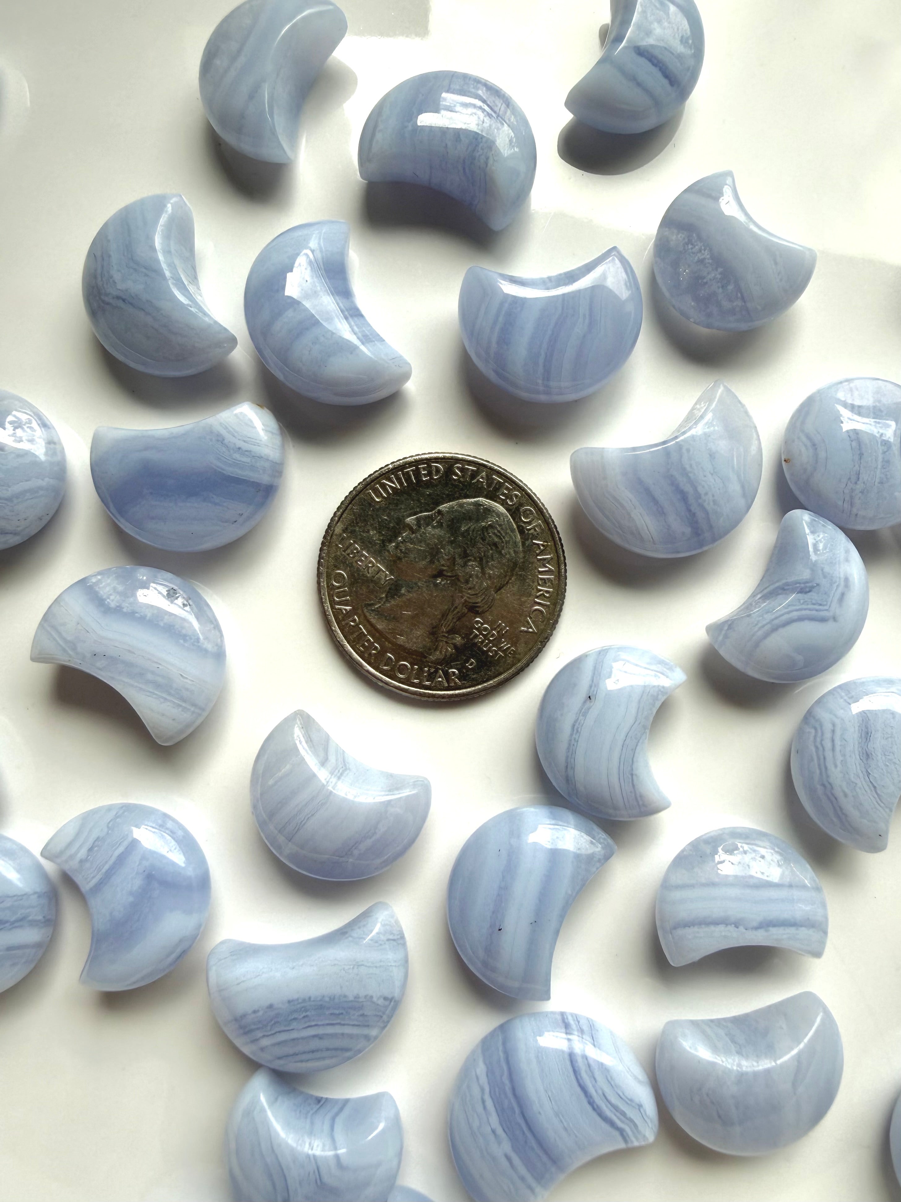Blue Lace Agate crescent moon carvings beside a U.S. quarter for size comparison