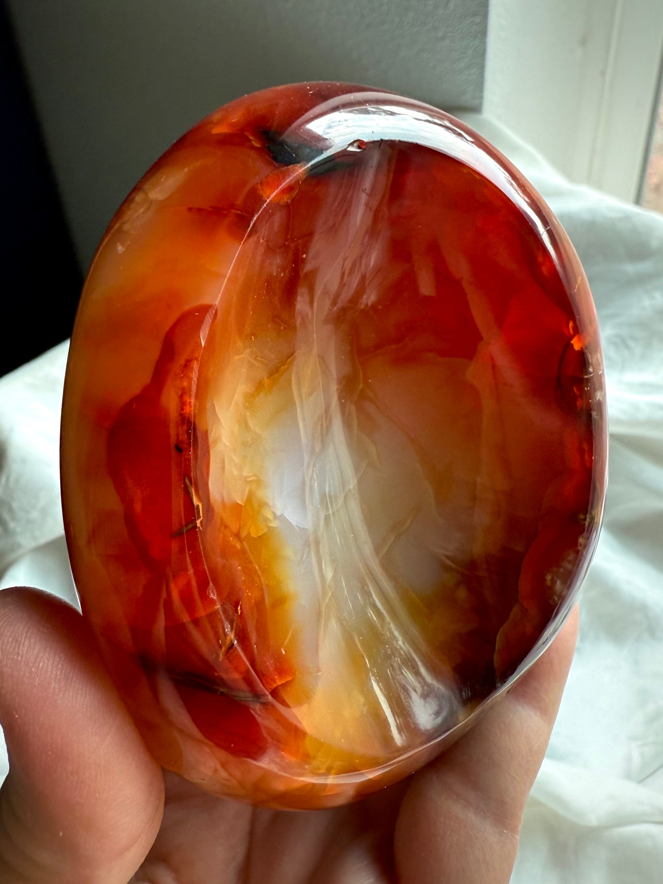 Polished Carnelian crystal bowl held in hand, showing curved side and rich orange-red banding.