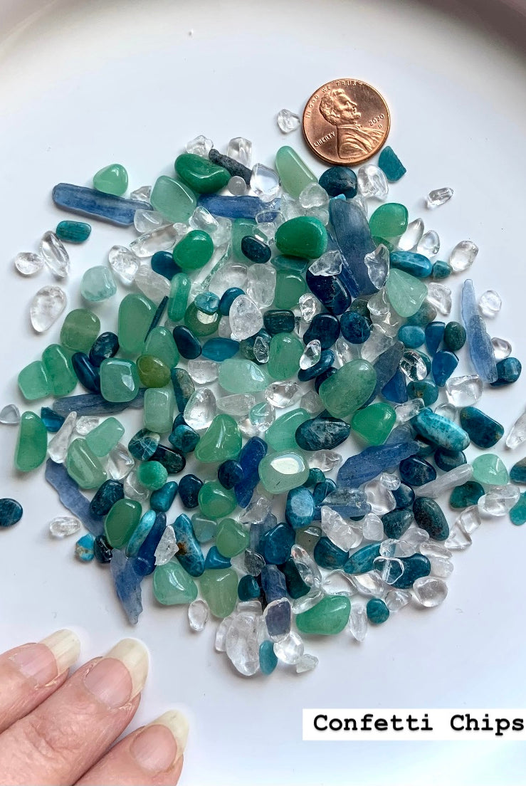 Showing the Mermaid Crystal Confetti Mix spread on a white plate with a penny and my hand for scale