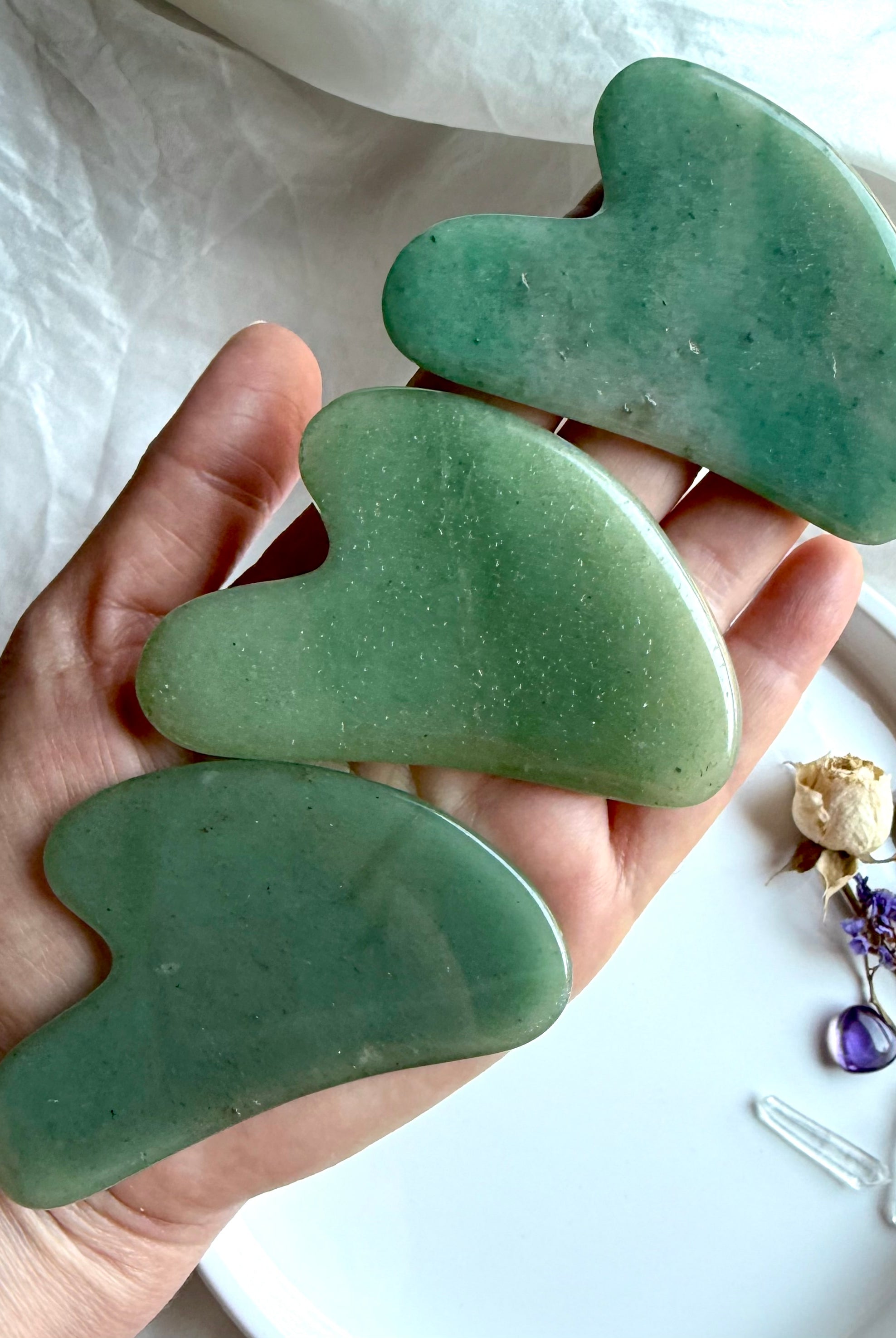 Hand holding three Green Aventurine crystal gua sha facial massage tools with smooth curved contour design