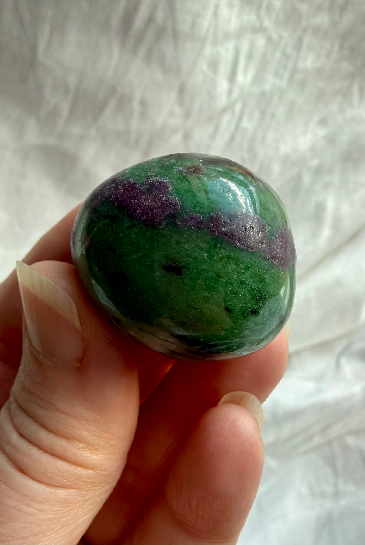 Ruby Zoisite tumbled crystal held between fingers, displaying deep green Zoisite, natural ruby inclusions and glossy polished finish