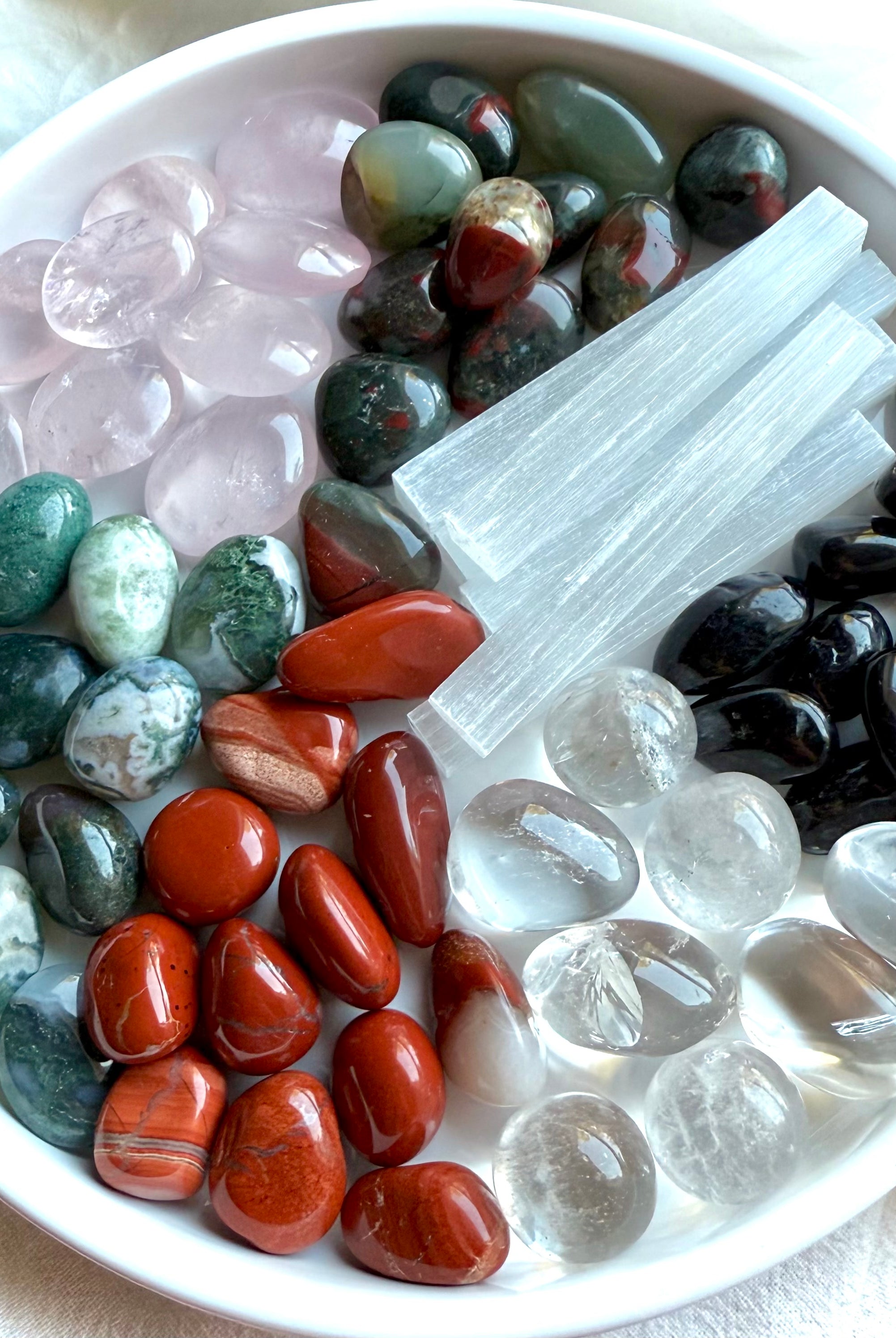 Variety of Bloodstone, Rose Quartz, Red Jasper, and more healing crystals on a white plate