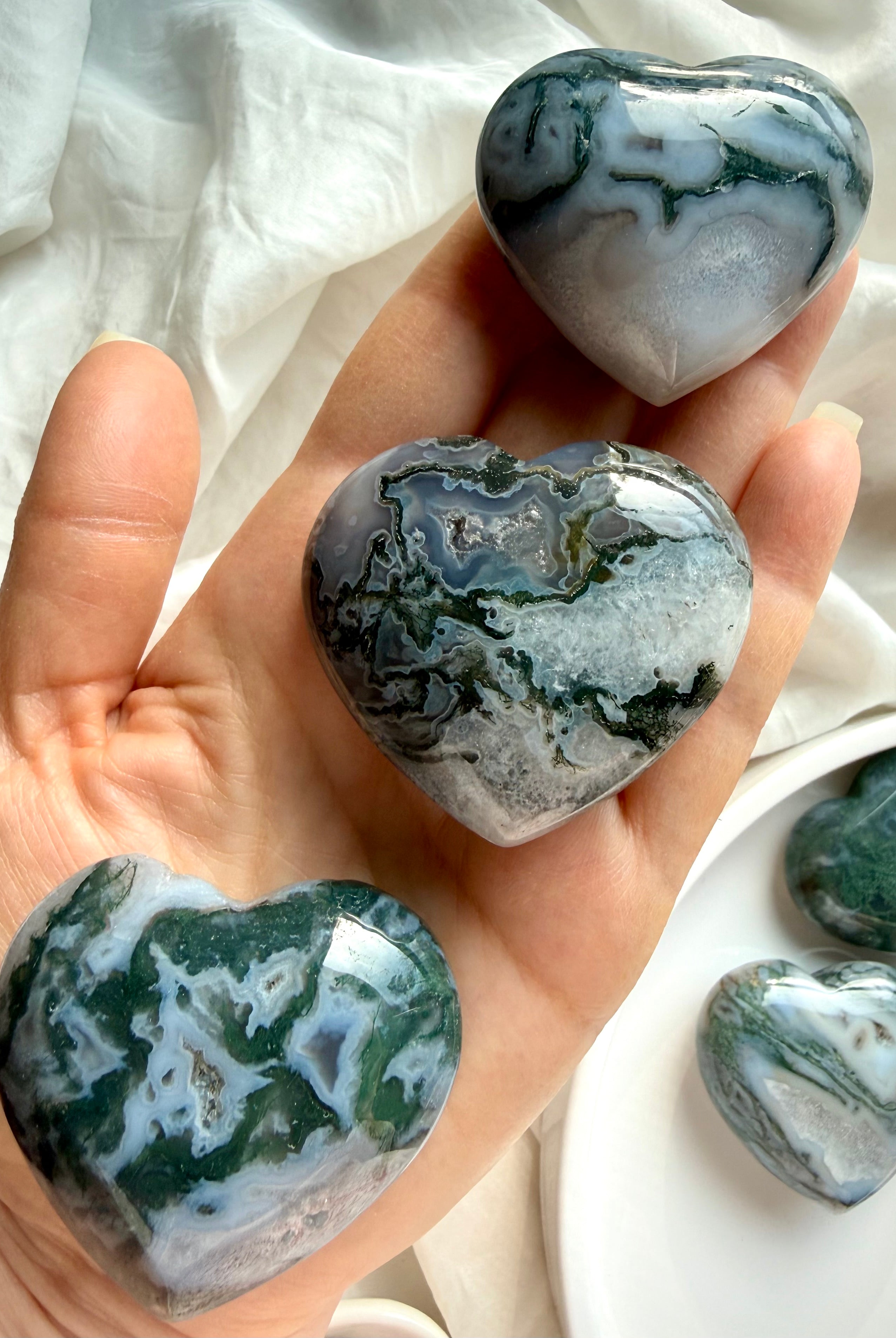 Closeup moss agate crystal hearts arranged on hand for scale with soft natural lighting highlighting green inclusions and patterns