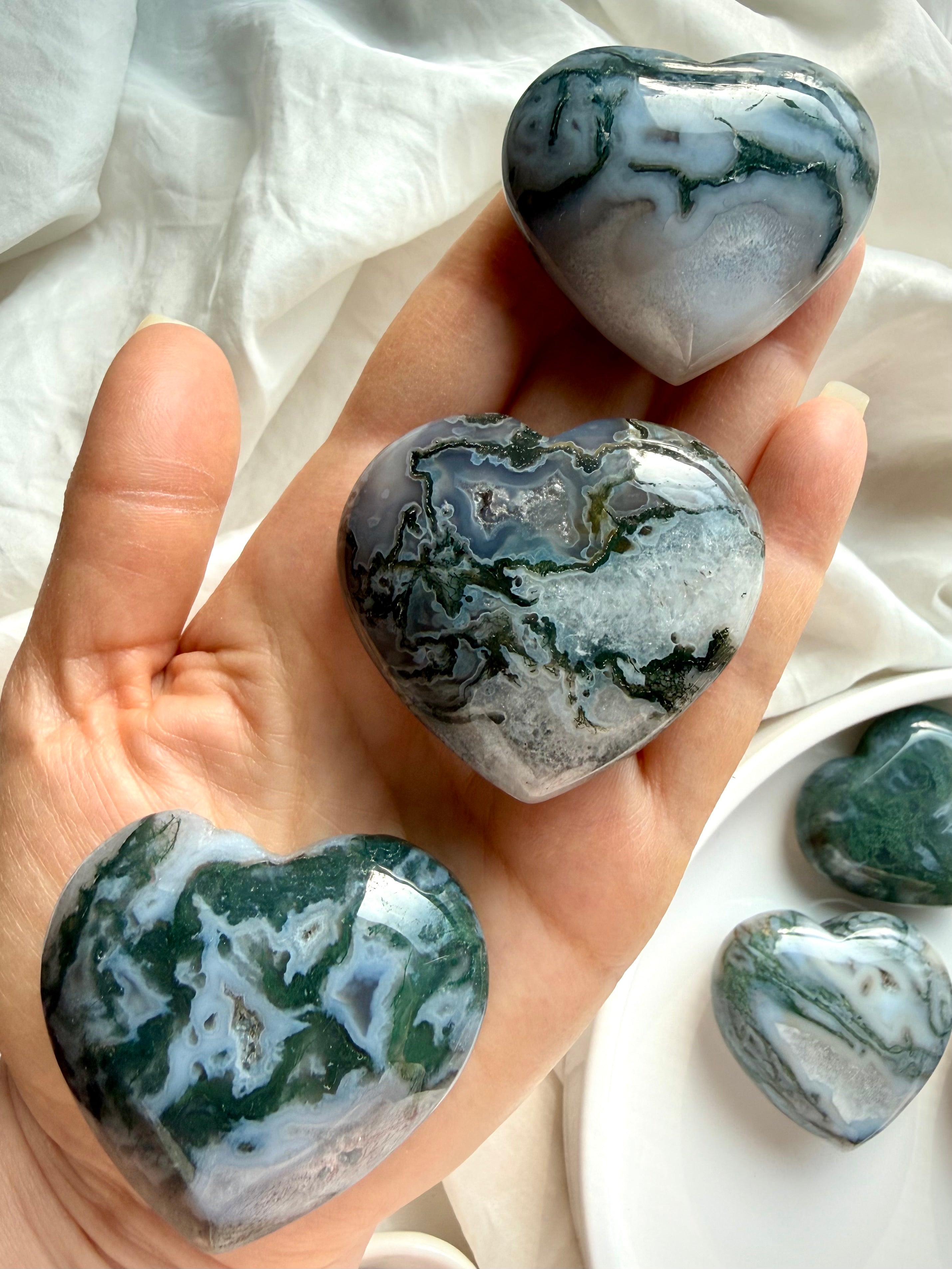 Closeup moss agate crystal hearts arranged on hand for scale with soft natural lighting highlighting green inclusions and patterns