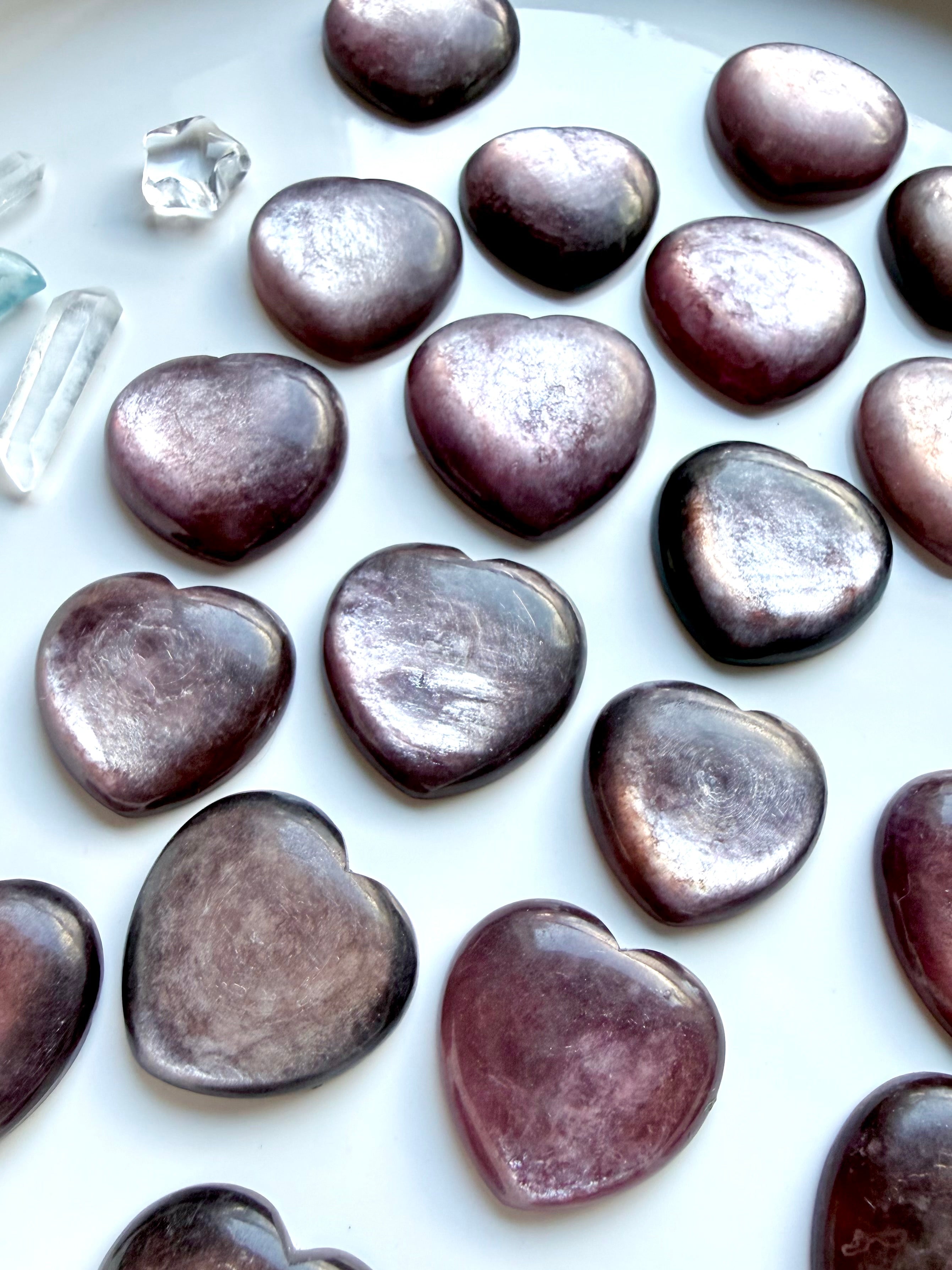 Gem Lepidolite hearts with mica shimmer on white tray, purple crystal heart carvings for calm and emotional healing