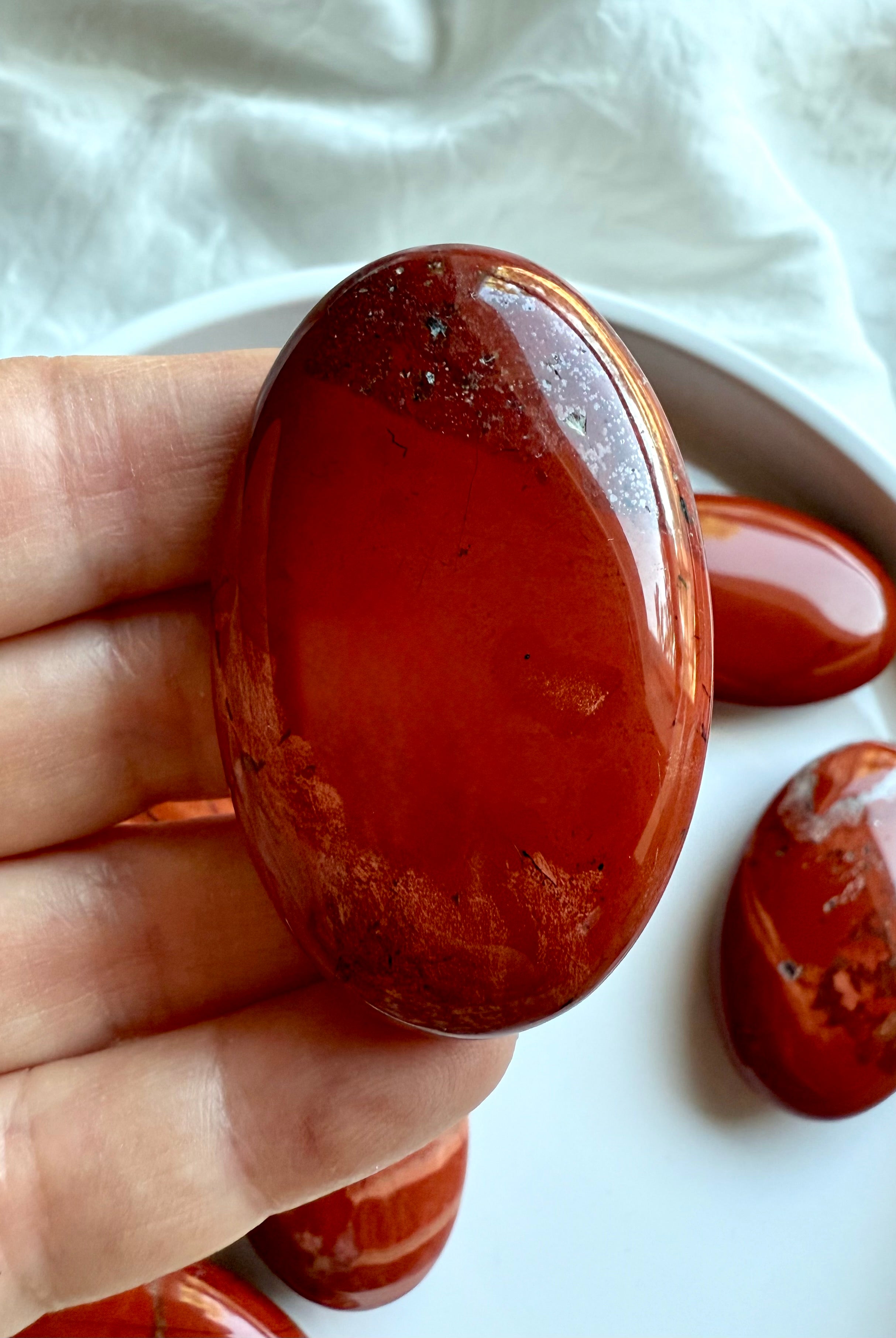 Closeup of oval Red Jasper palm stone — Root Chakra healing crystal for grounding and resilience.