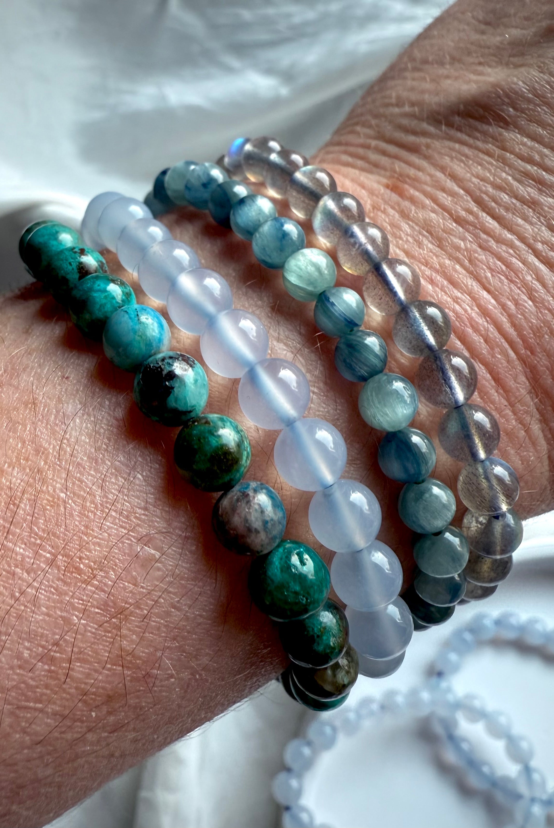 Stacked crystal bracelets on wrist including Blue Chalcedony, Chrysocolla, Aquamarine, and Labradorite — gemstone stack for serenity and balance.