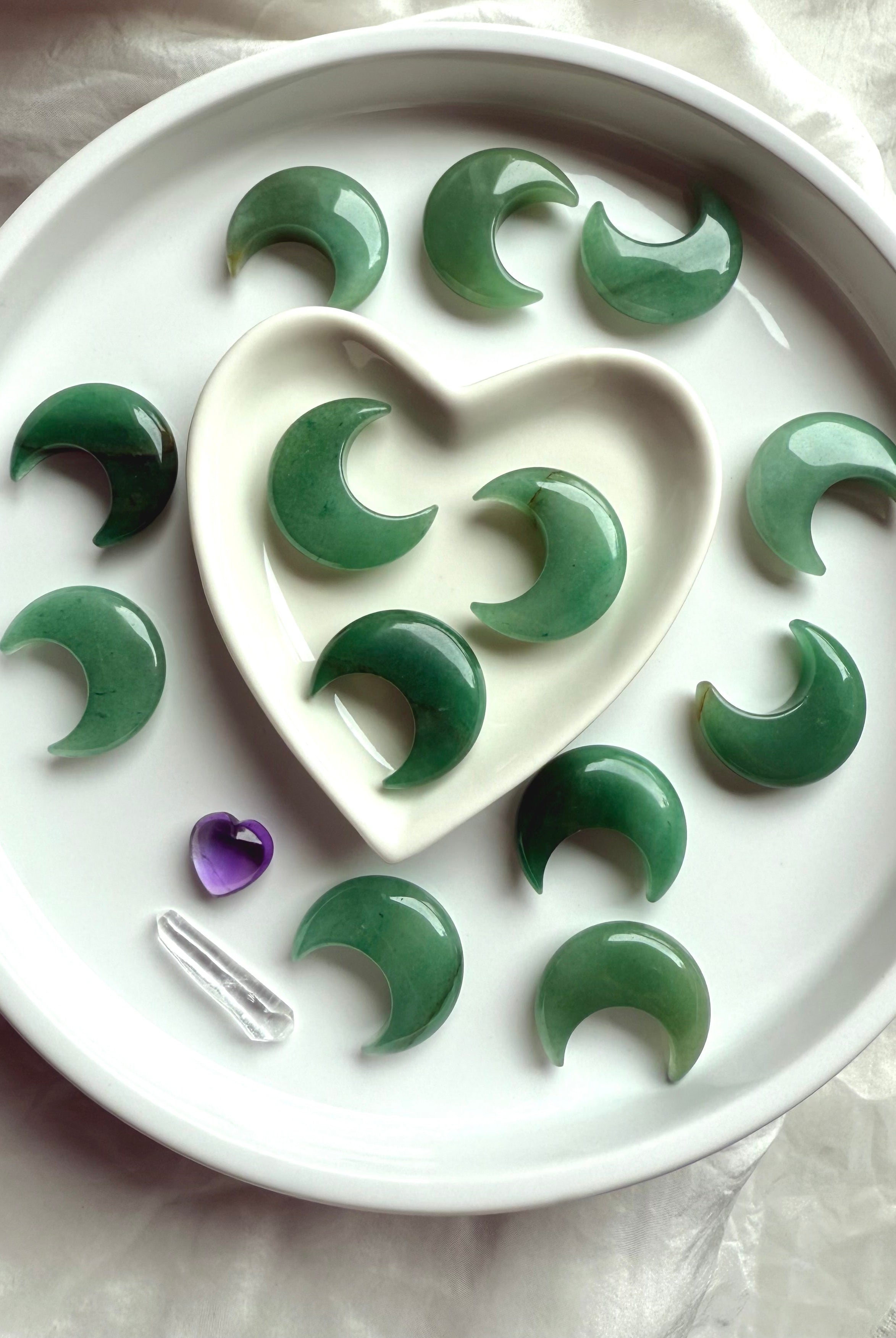 Wide view of Green Aventurine moons in a white heart bowl with additional moons surrounding, altar décor for Heart Chakra energy