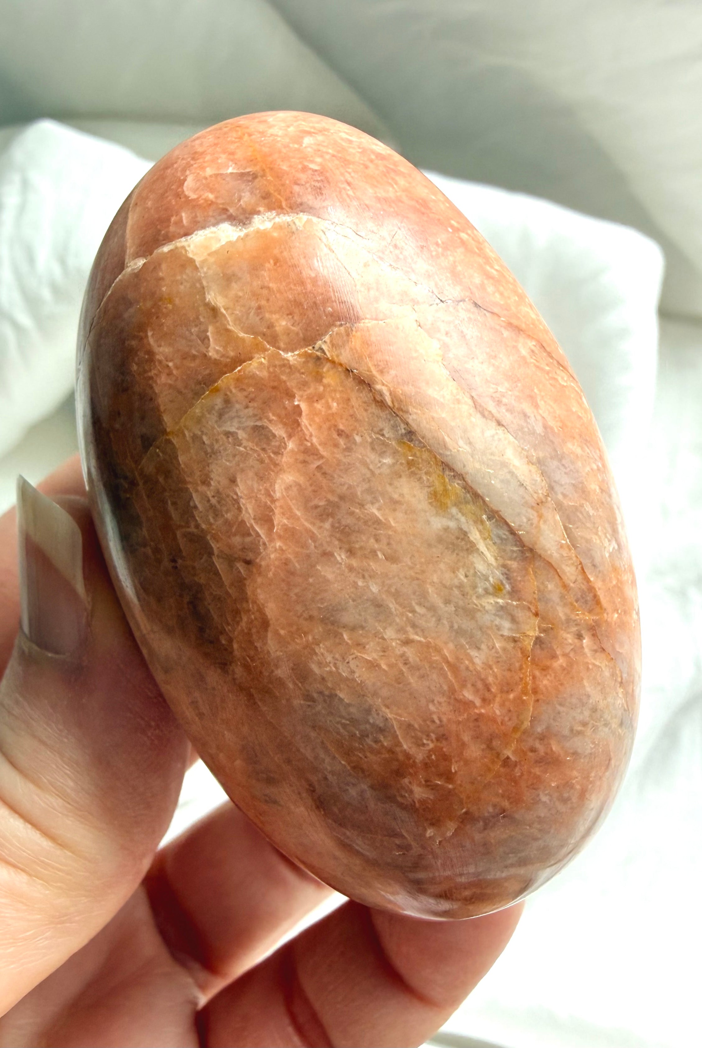 Hand holding a polished Peach Moonstone palm stone with soft natural shimmer and warm earthy peach coloring