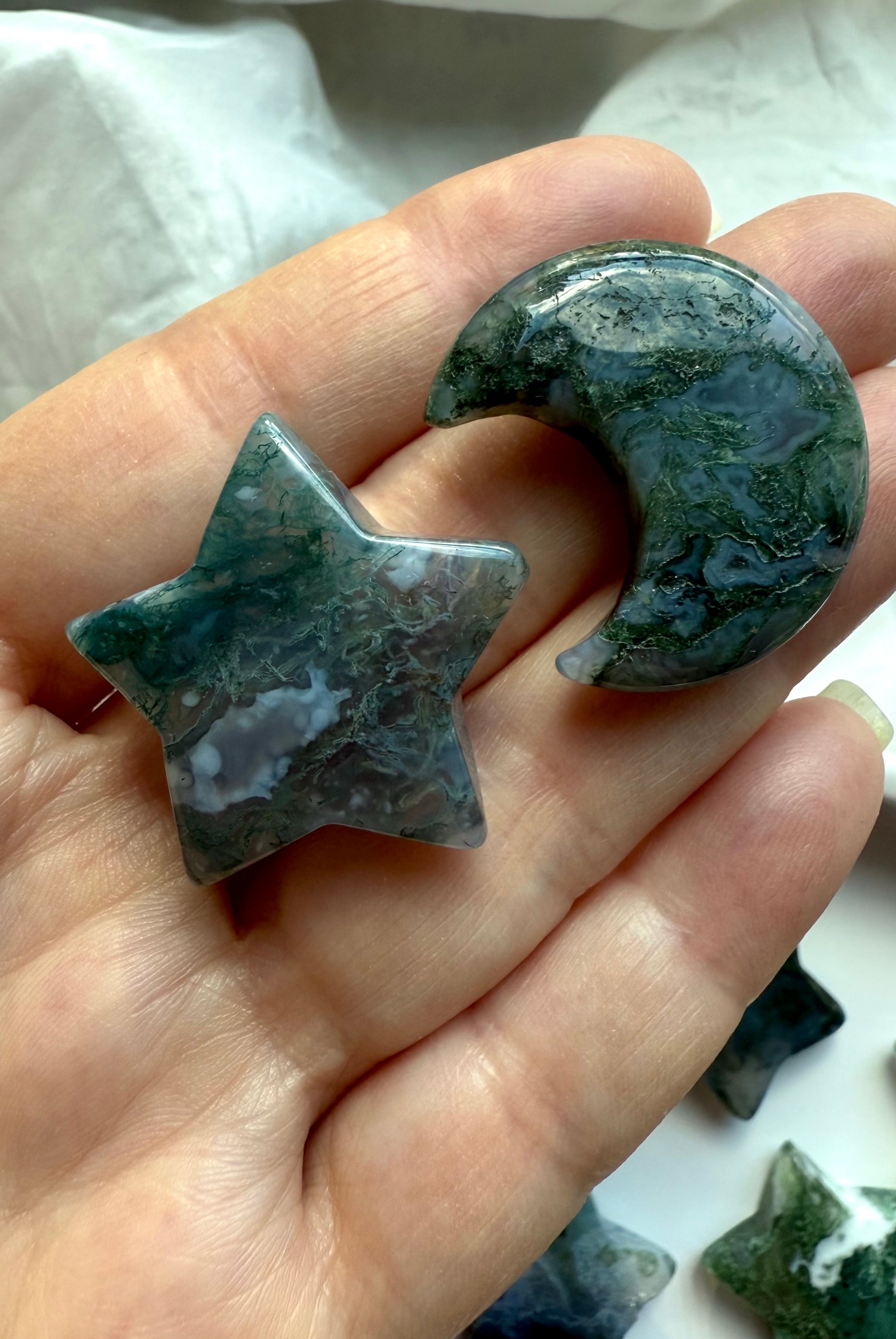 Moss Agate star and crescent moon shown in hand, highlighting organic green inclusions and translucency — grounding crystal carvings for heart-centered healing.