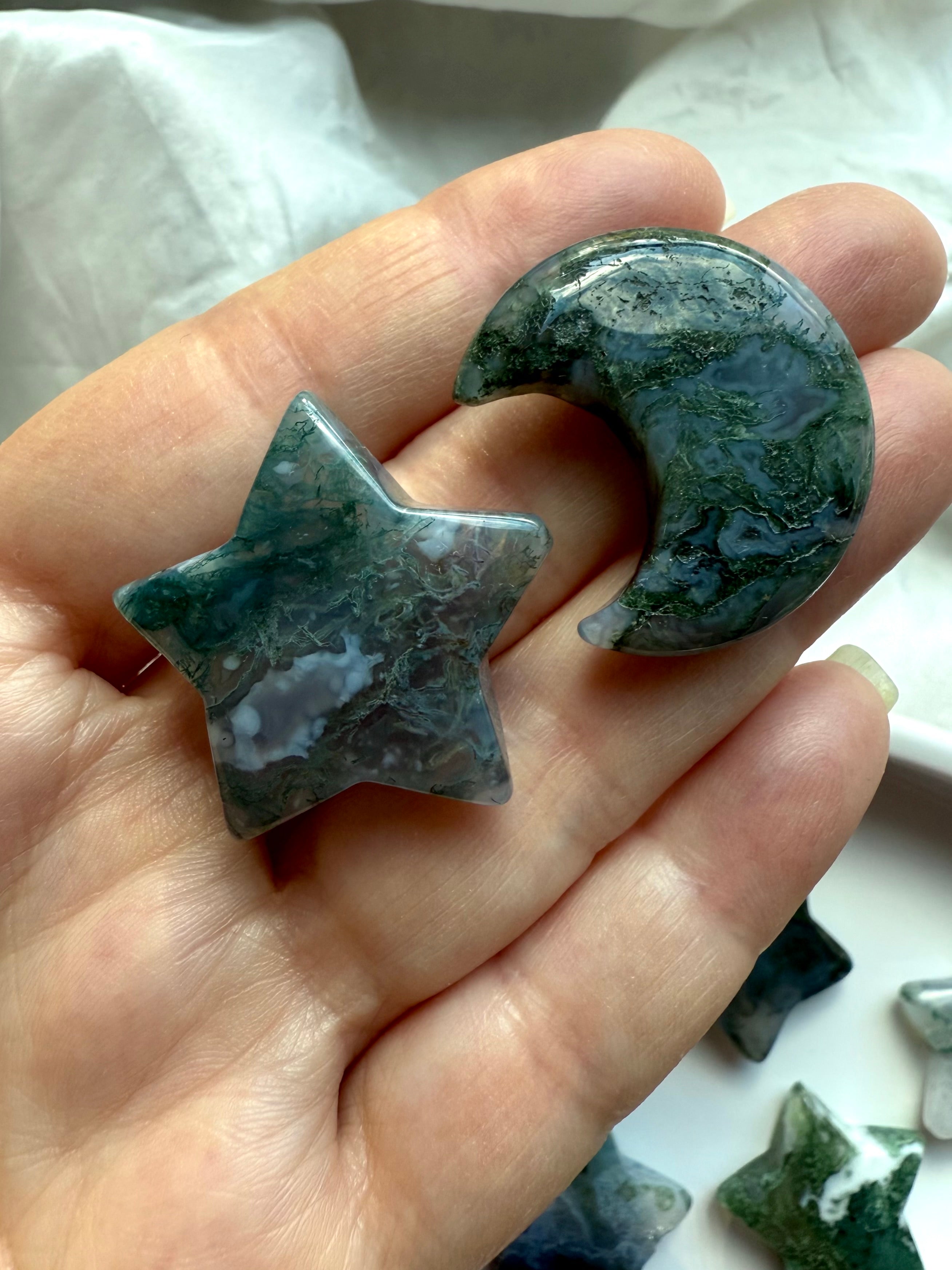 Moss Agate star and crescent moon shown in hand, highlighting organic green inclusions and translucency — grounding crystal carvings for heart-centered healing.