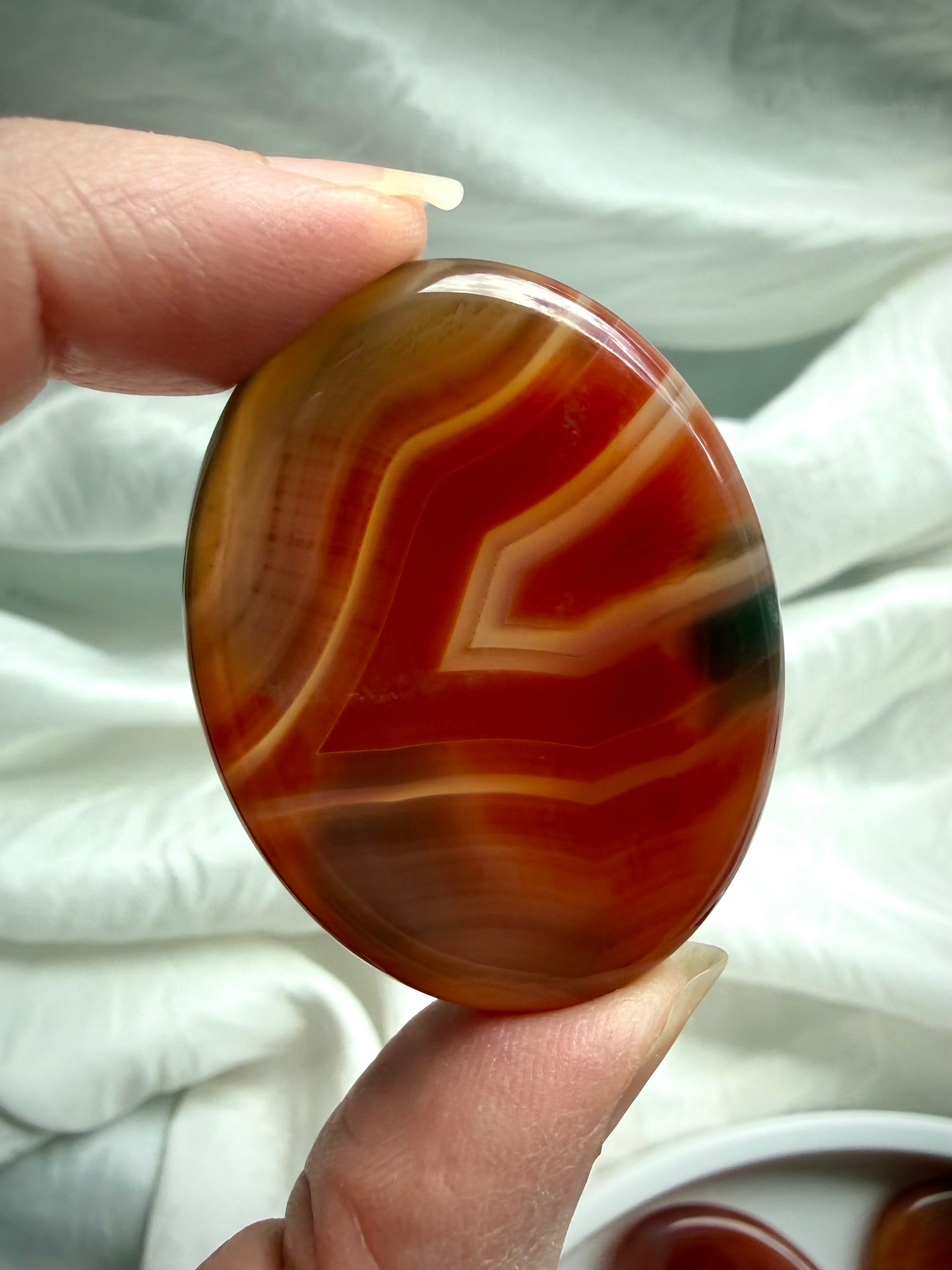 Banded Carnelian worry stone with deep red and golden translucent layers, polished oval thumb stone for meditation
