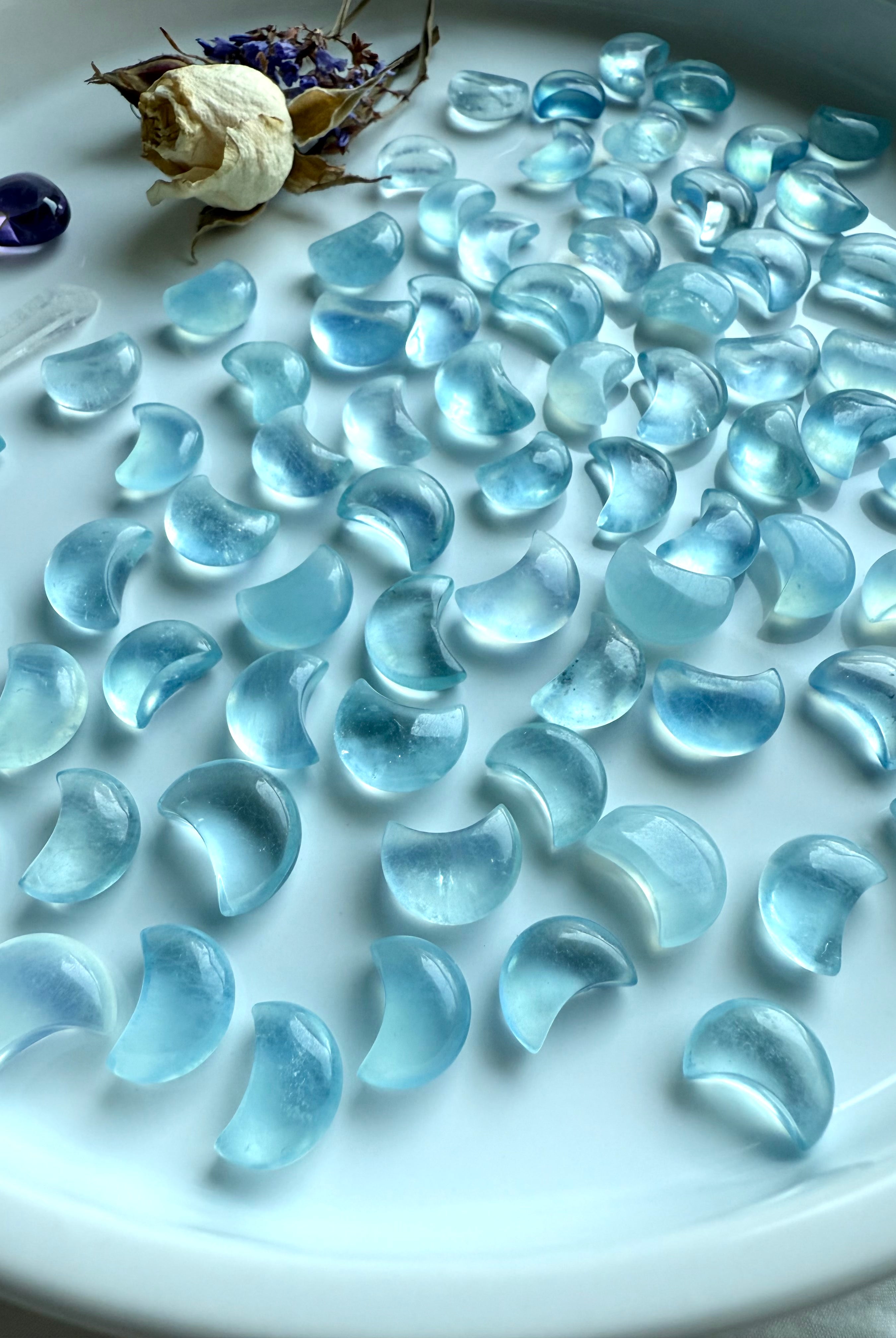 Angled side view of Aquamarine Mini Moons on a white tray with dried botanicals — gemstone moon carvings with soft translucent energy