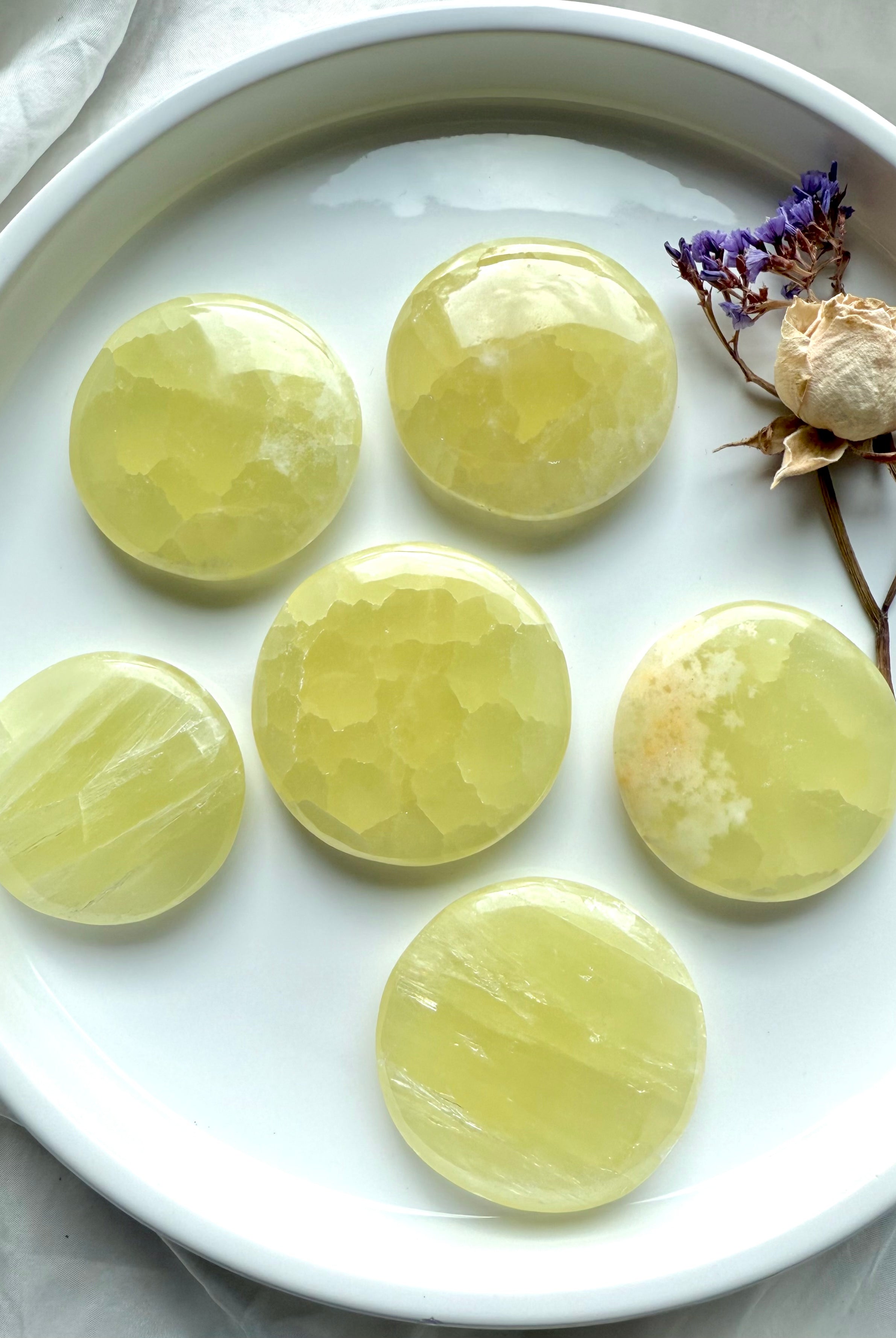 Round yellow calcite palm stones displayed in a tray with dried flowers and quartz