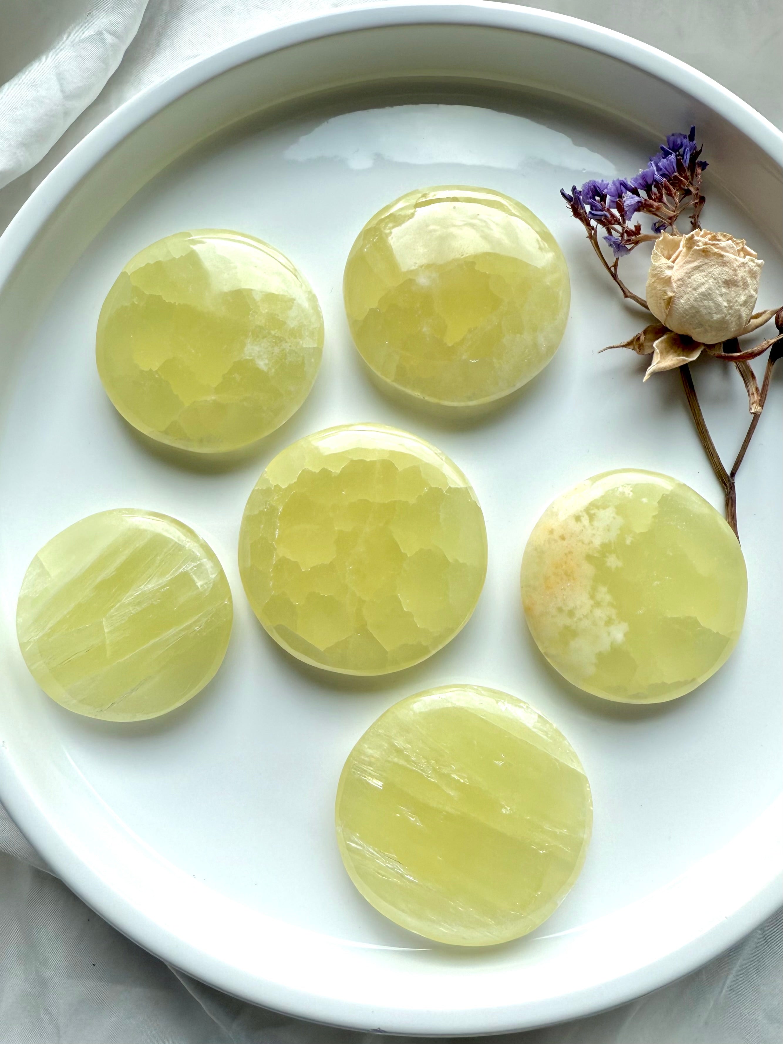 Round yellow calcite palm stones displayed in a tray with dried flowers and quartz