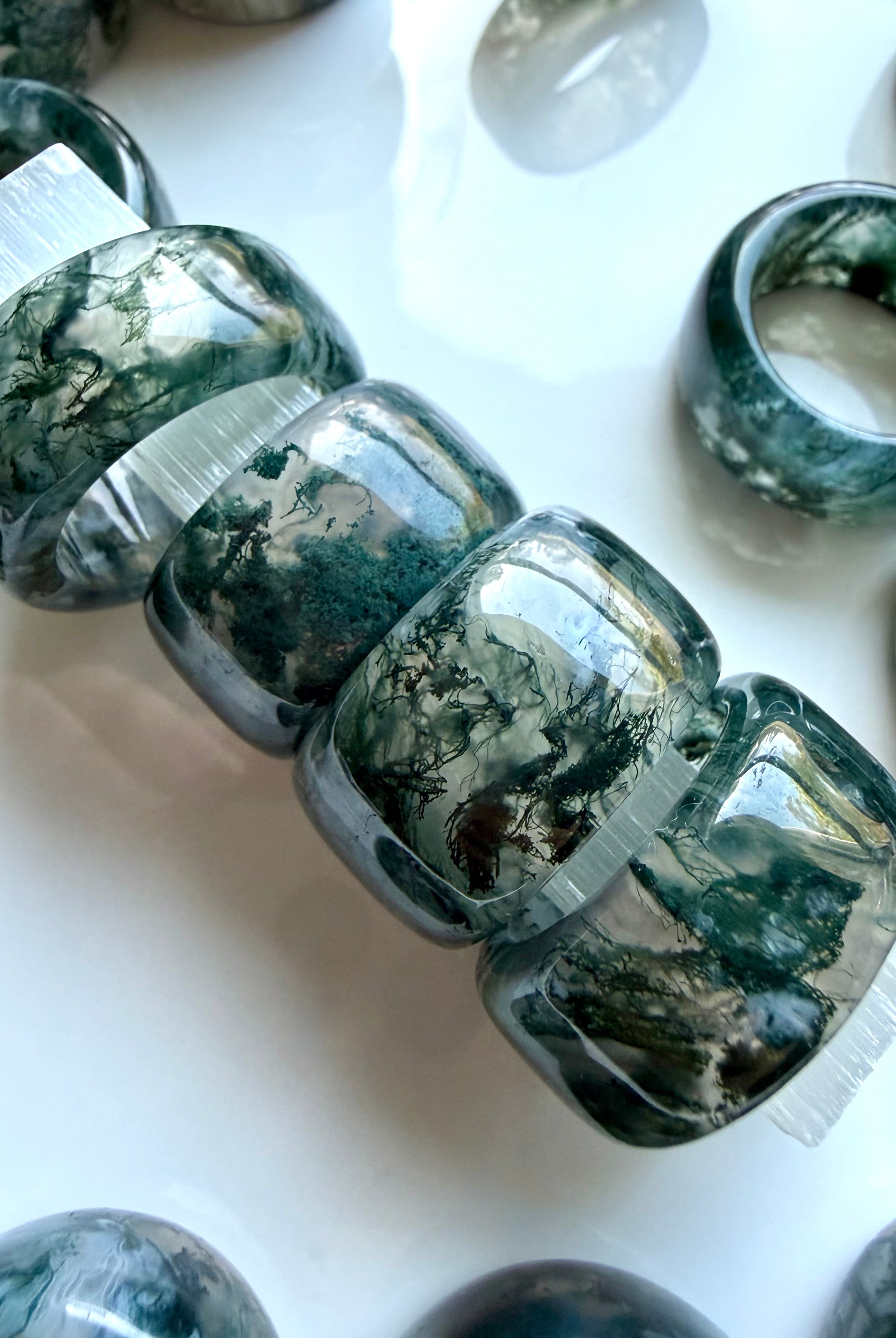 stacked moss agate wide band crystal rings showing natural landscape inclusions and earthy organic patterning