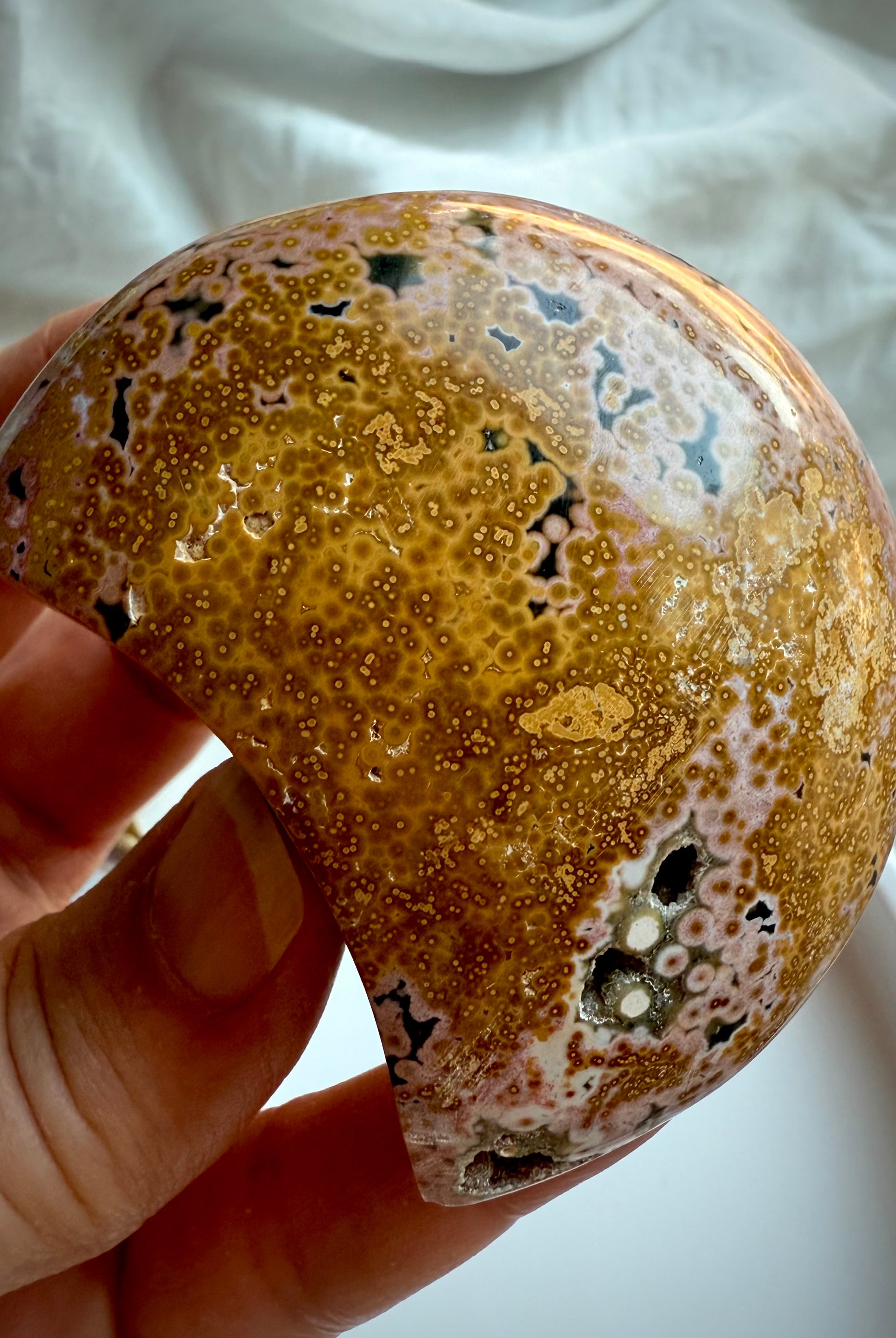 Golden yellow and peach Ocean Jasper moon with intricate orbicular texture and natural vugs held in hand