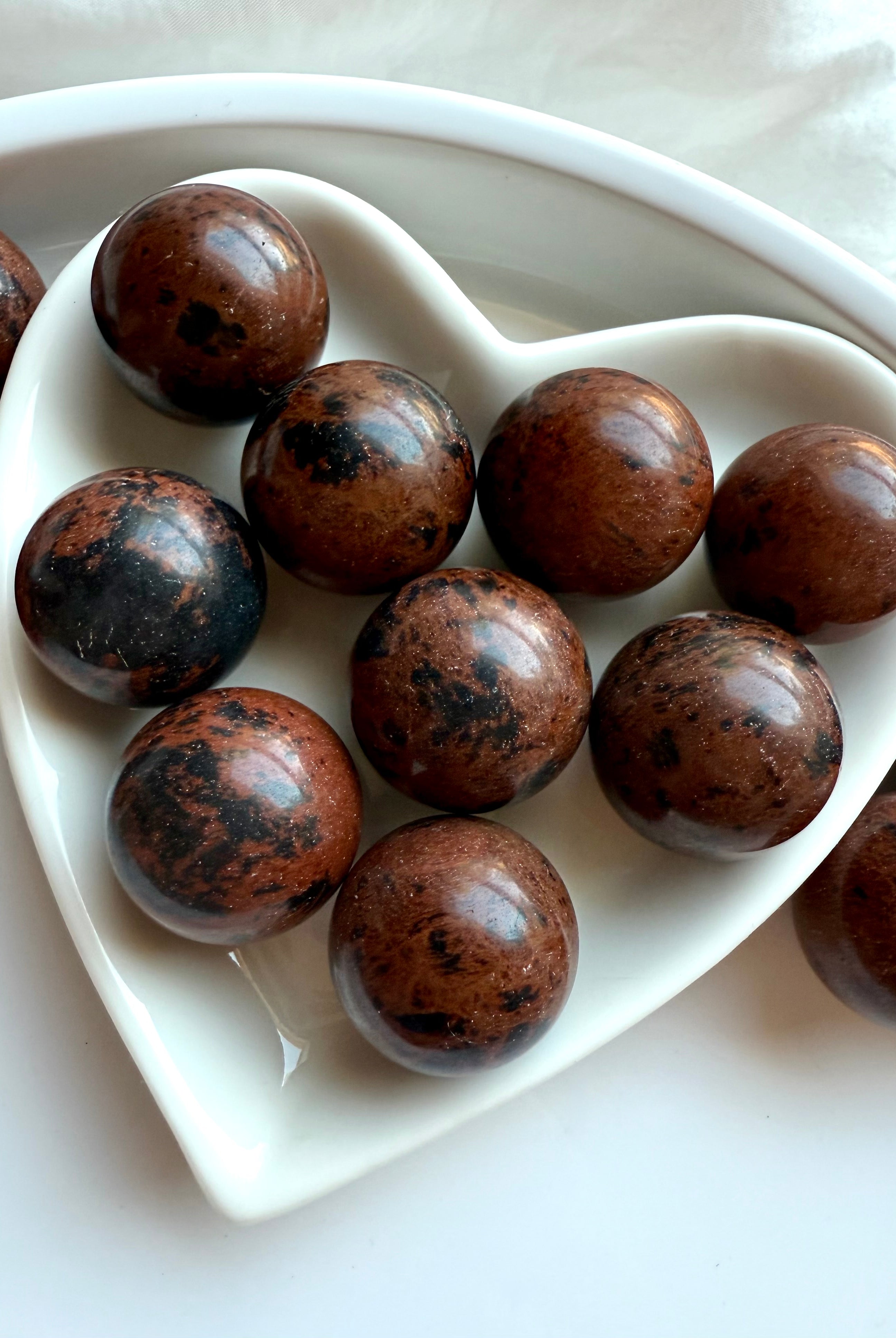 Close up of Mahogany Obsidian mini spheres arranged in white dish – protective healing crystals with natural inclusions