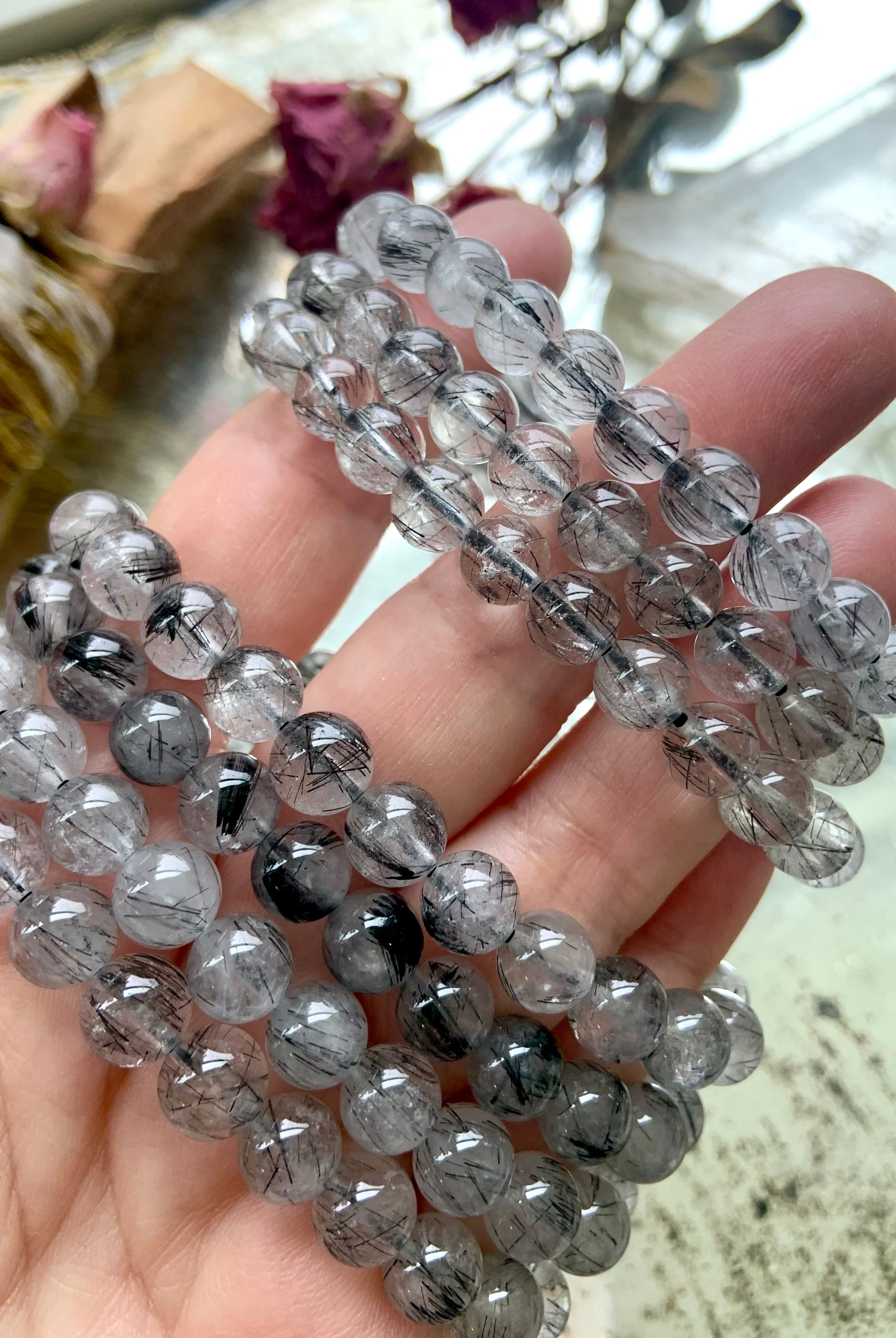 Closeup of a stack of Black Tourmaline in Quartz bracelets on a hand over a mirrored surface, showcasing the clarity and fine tourmaline inclusions