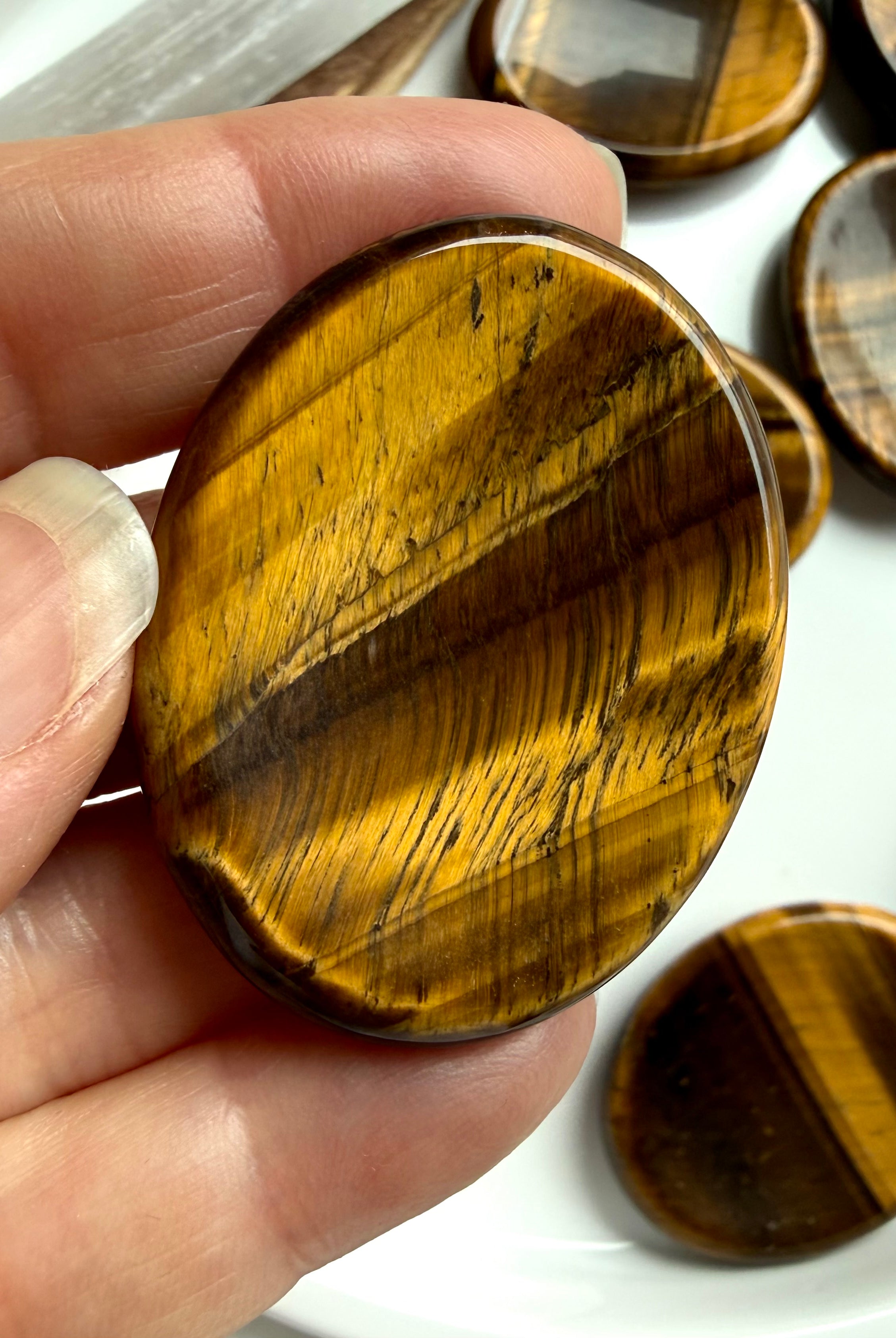 tiger’s eye worry stone held between fingers showing natural banding and sheen, crystal for protection strength and balance