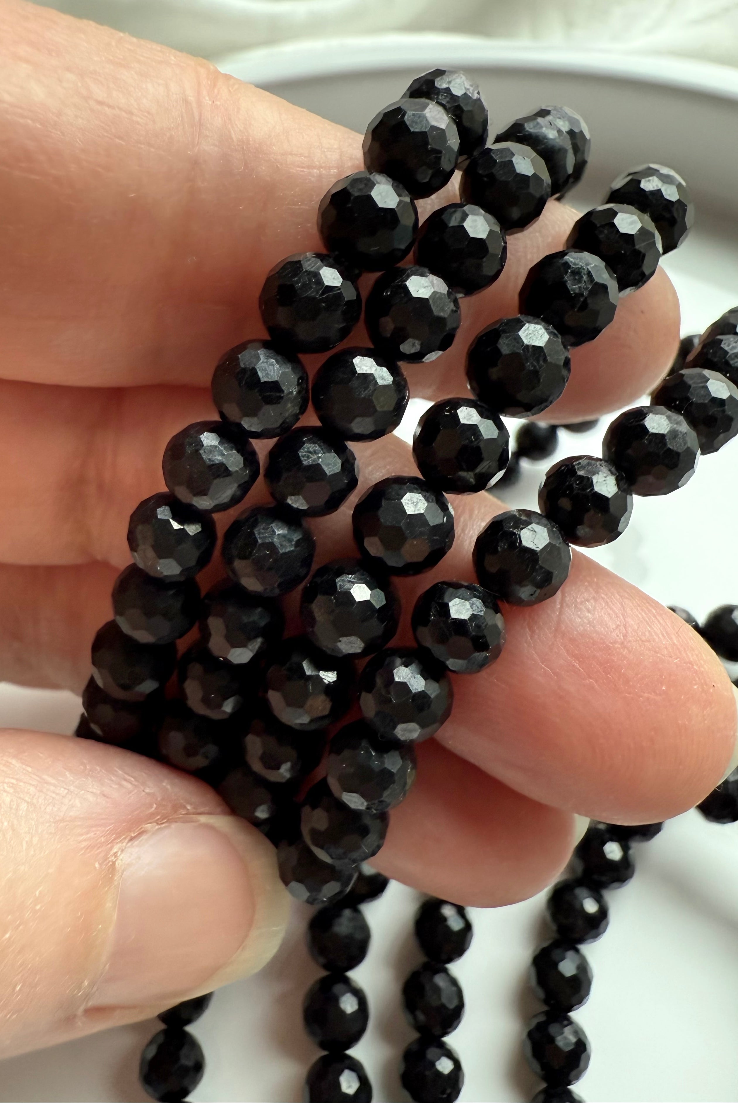 fingers holding strands of faceted black tourmaline crystal beads with glossy reflective surface