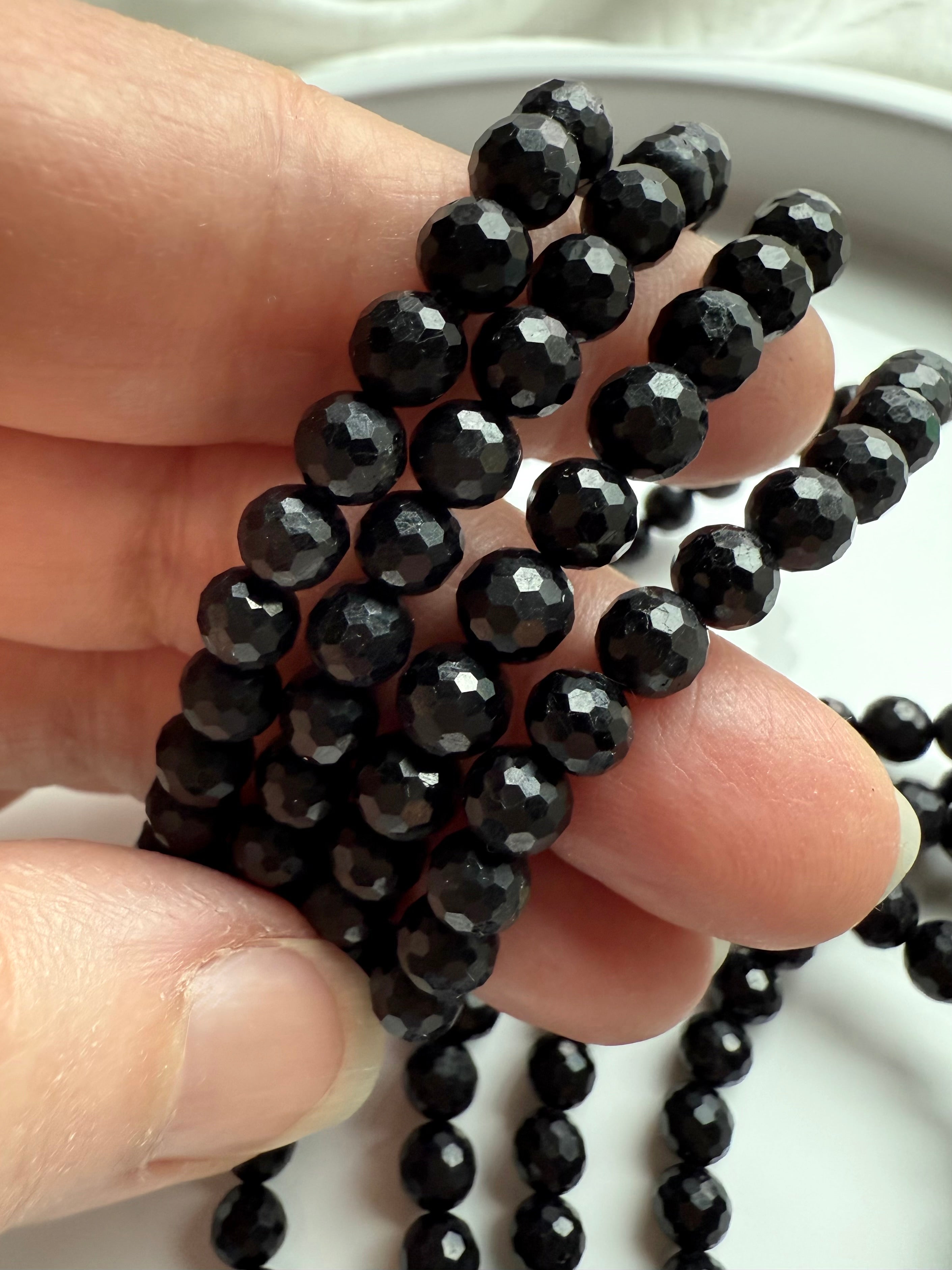 fingers holding strands of faceted black tourmaline crystal beads with glossy reflective surface