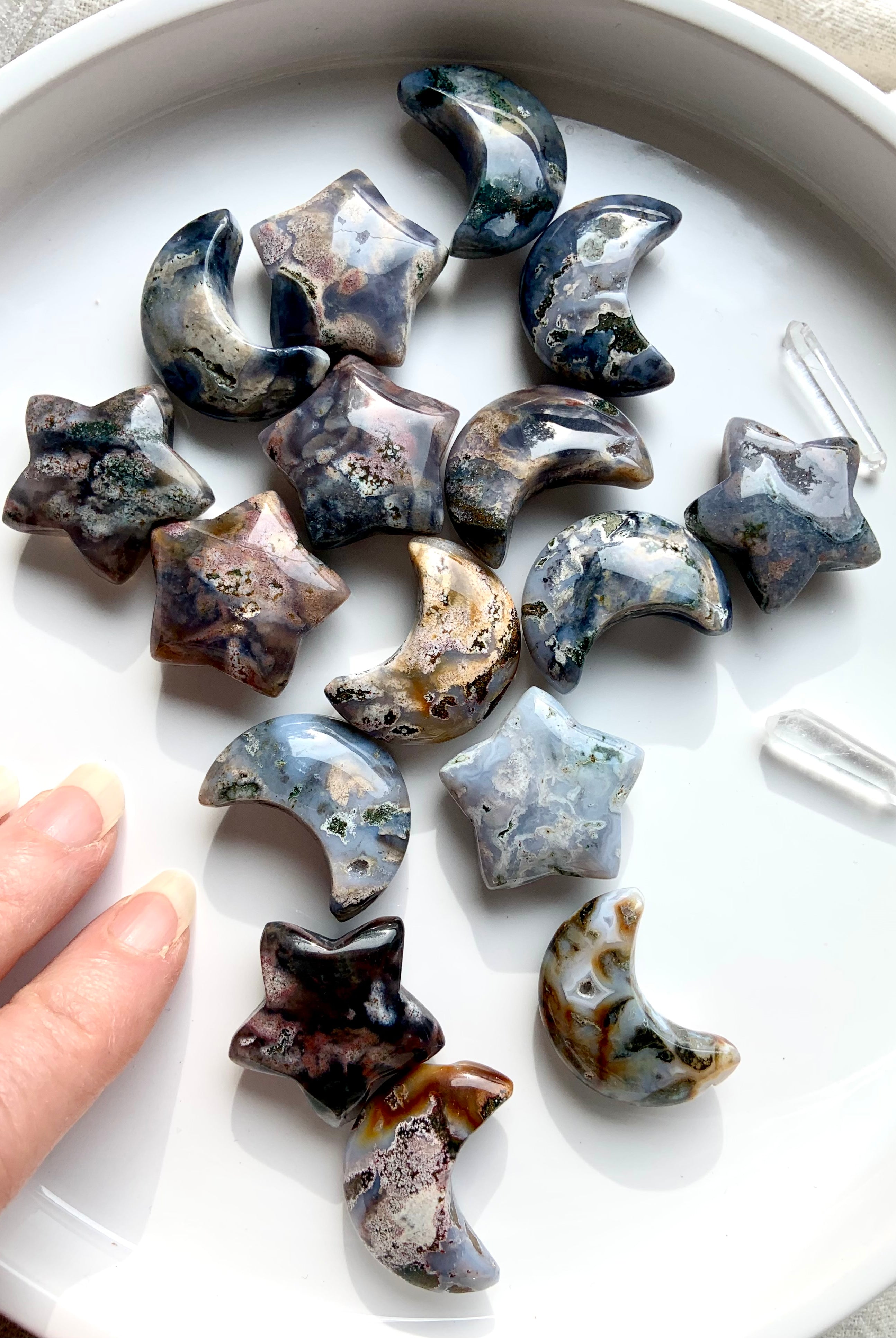 Cosmic Ocean Jasper moons and stars with quartz points on white dish and hand reaching in, celestial healing crystal carvings for rituals