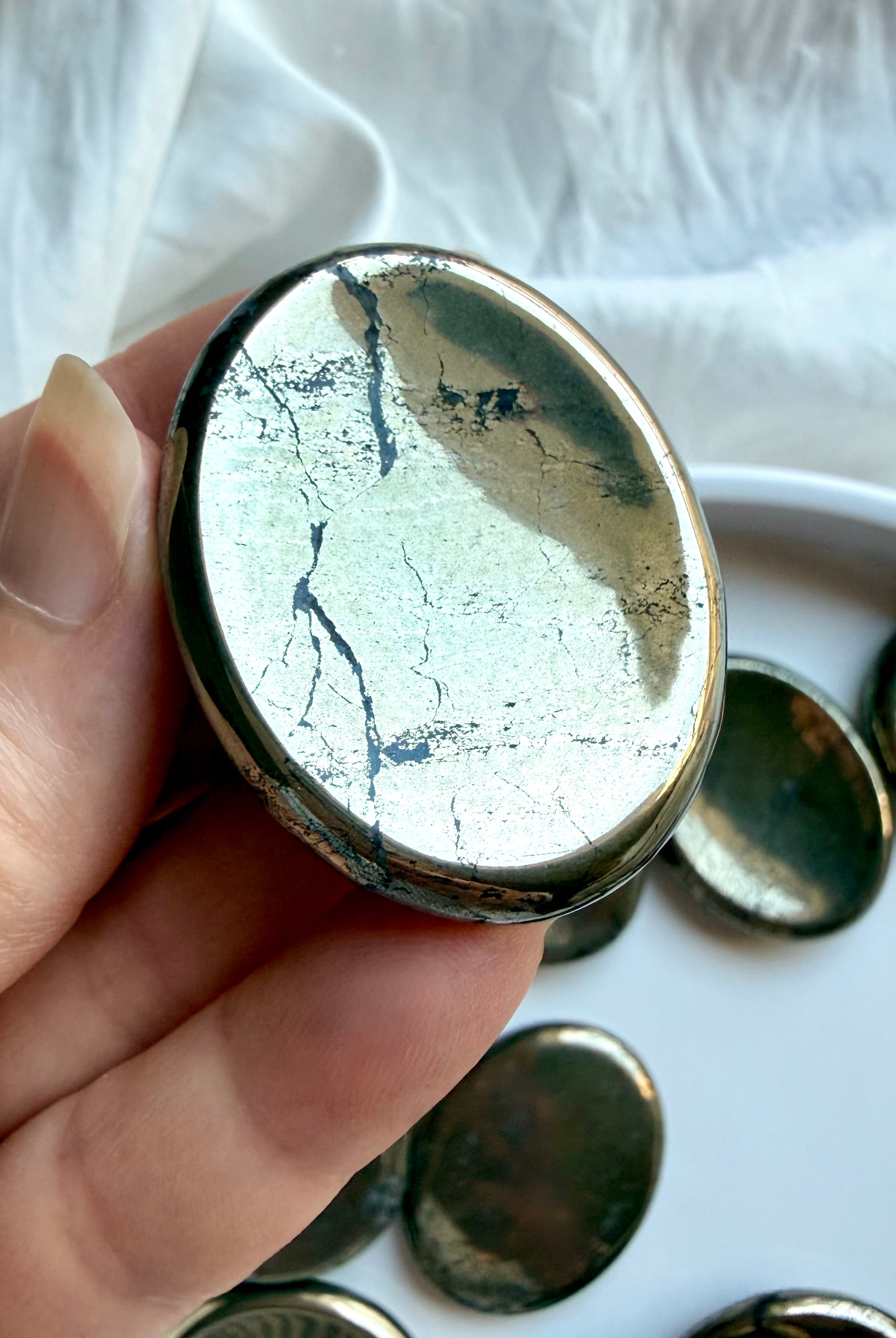 Polished Pyrite thumb stone held in hand with bright metallic luster and natural mineral patterning