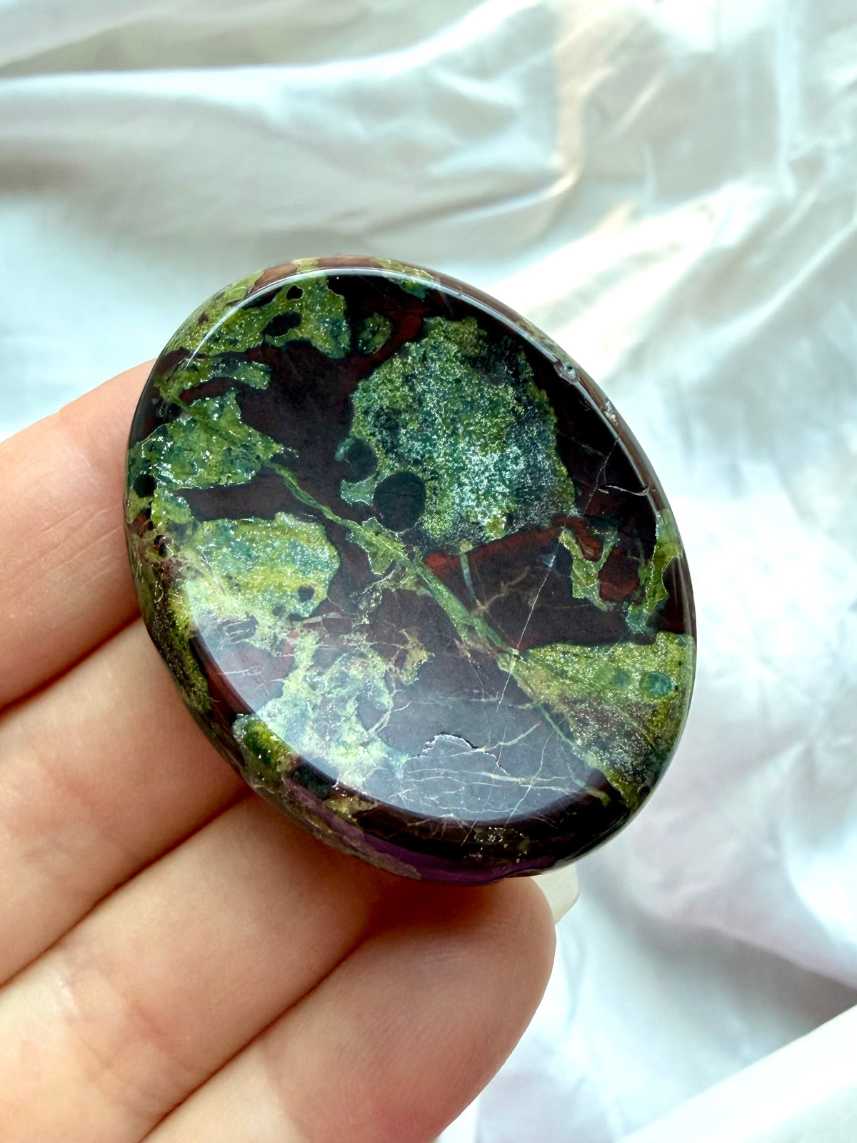 Close-up of Dragon Blood Stone crystal worry stone with dramatic forest-green and burgundy patterns for courage and emotional strength