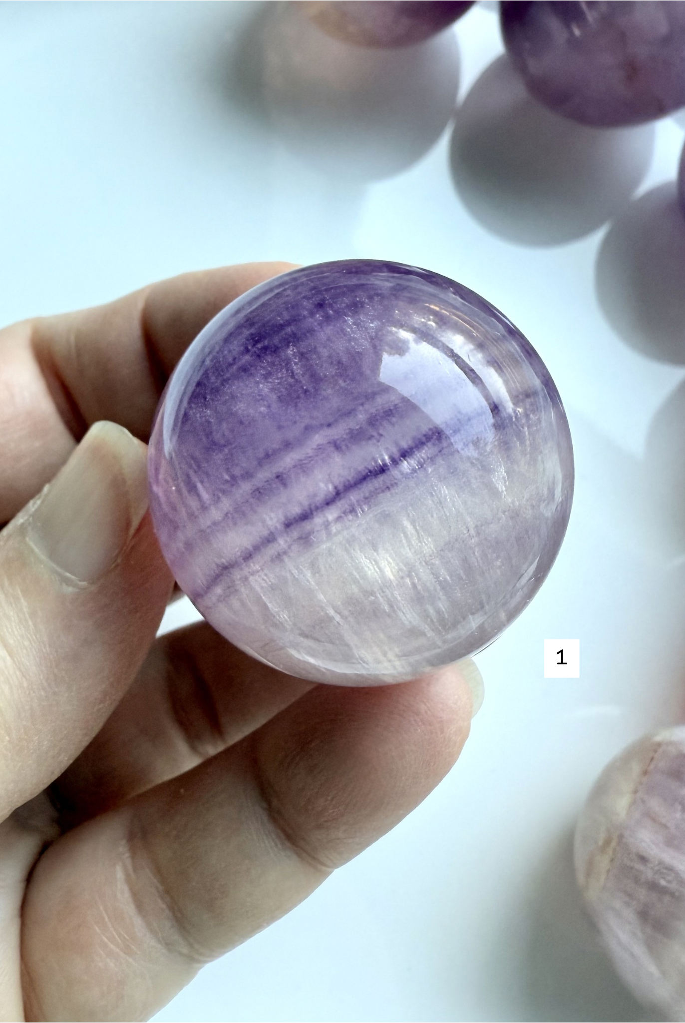 hand holding Silky Magenta Fluorite sphere with luminous purple banding and glossy polished finish