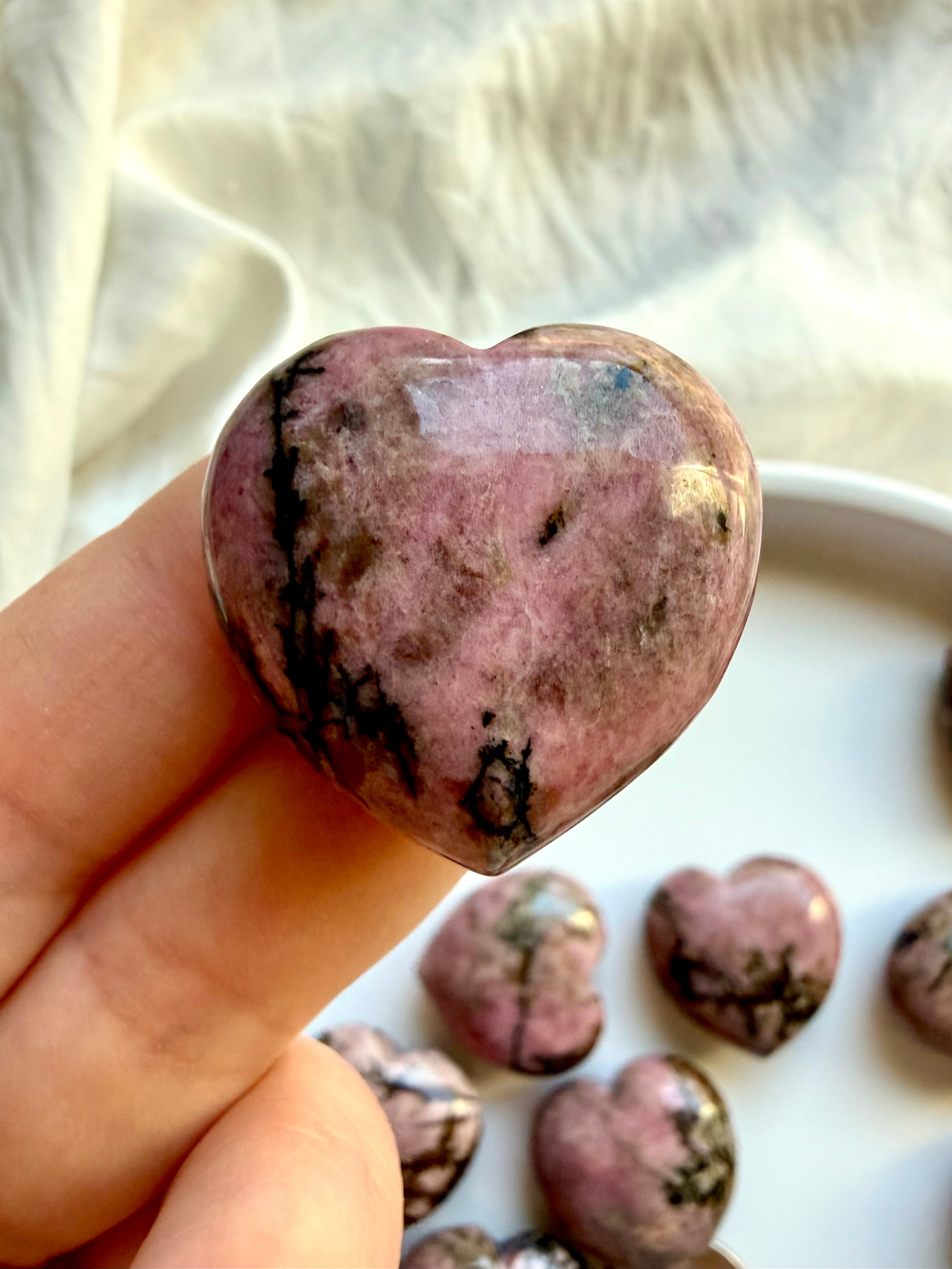 Closeup Pink Rhodonite heart held in hand with black manganese inclusions and polished crystal finish