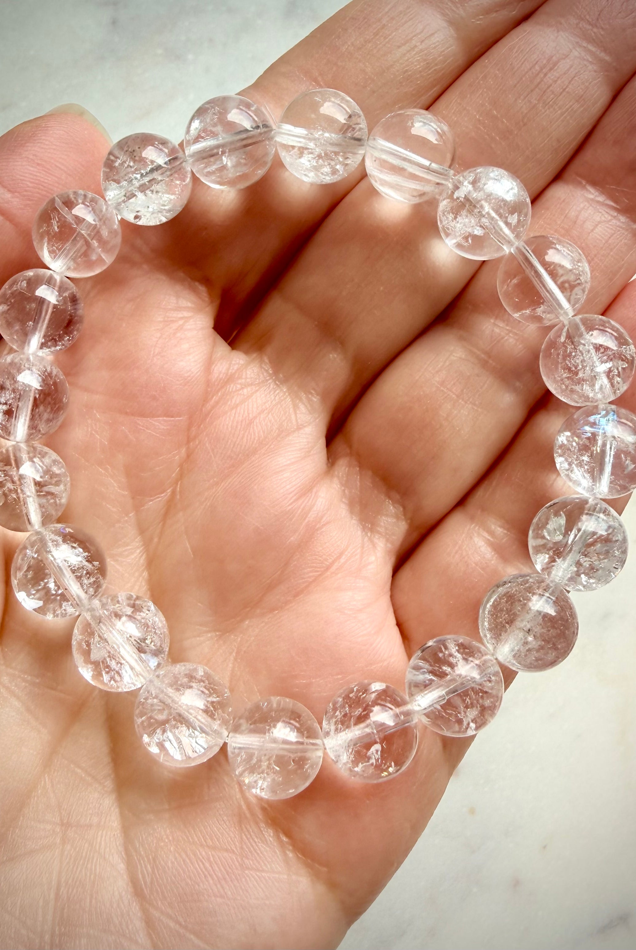 Clear Quartz crystal bracelet held in hand with transparent polished beads and light-catching flashes