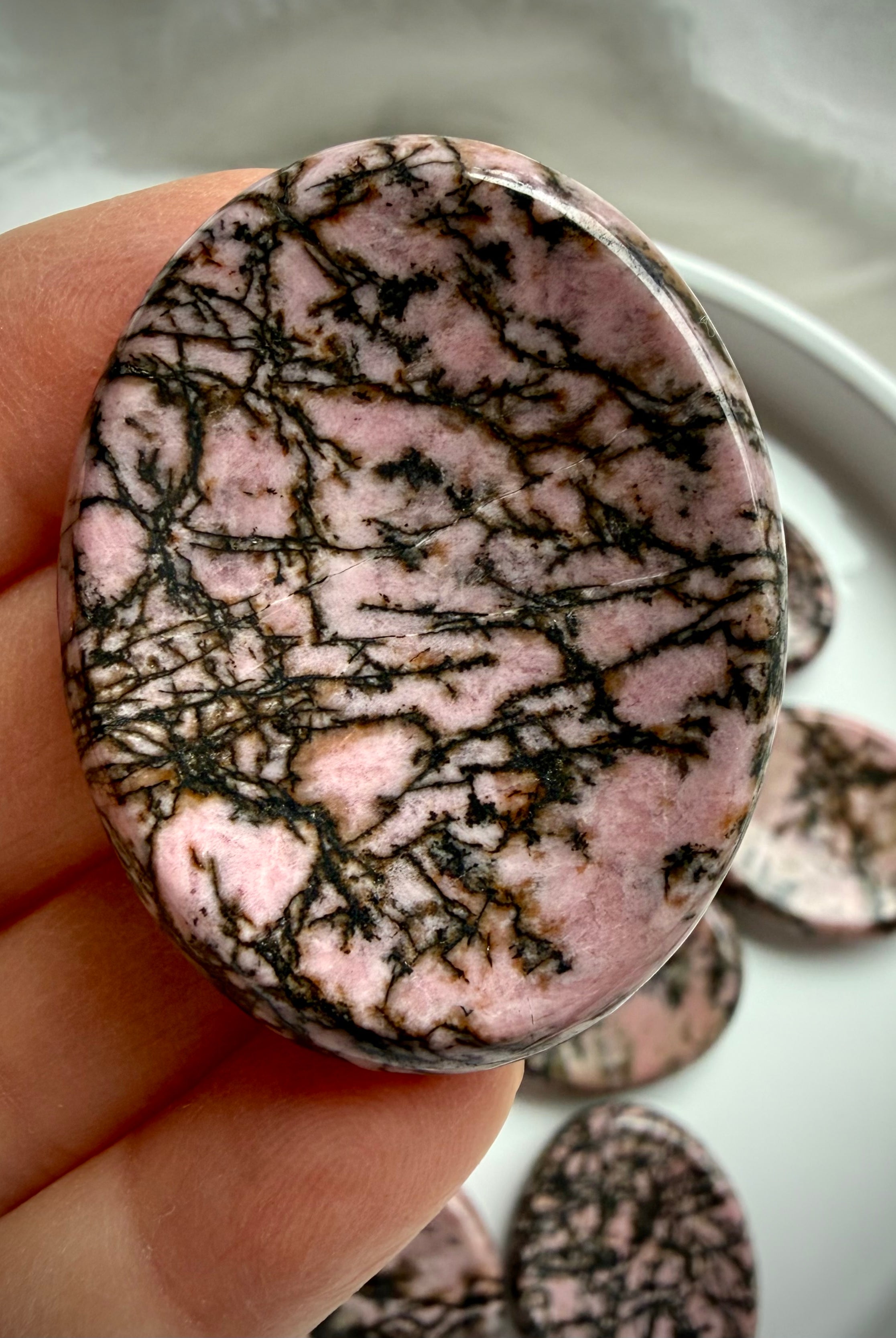 Rhodonite worry stone in hand showing varied black spiderweb patterns running through pink matrix
