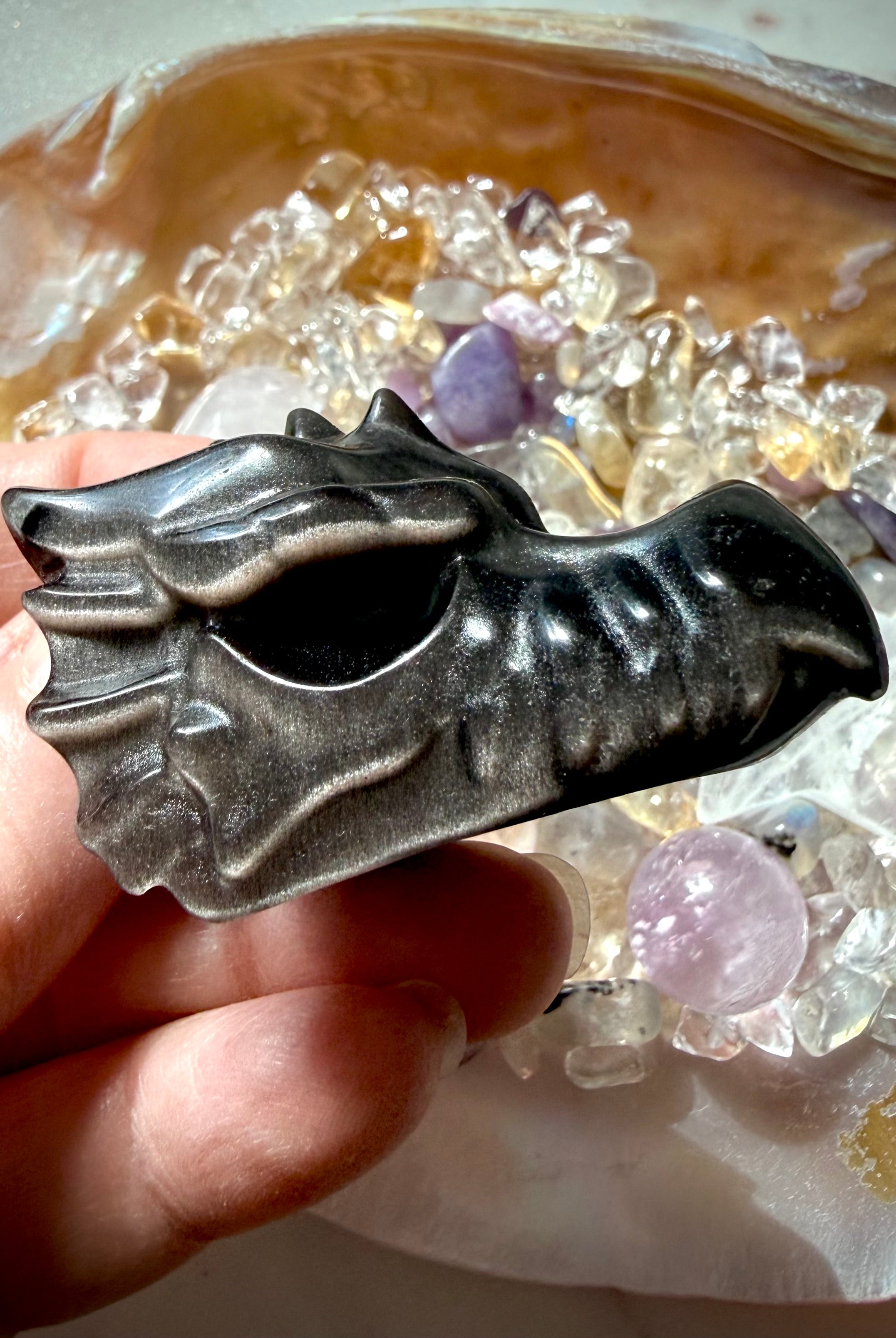 silver sheen obsidian dragon carving displayed on shell dish of crystals highlighting reflective sheen, crystal for shadow work and intuition