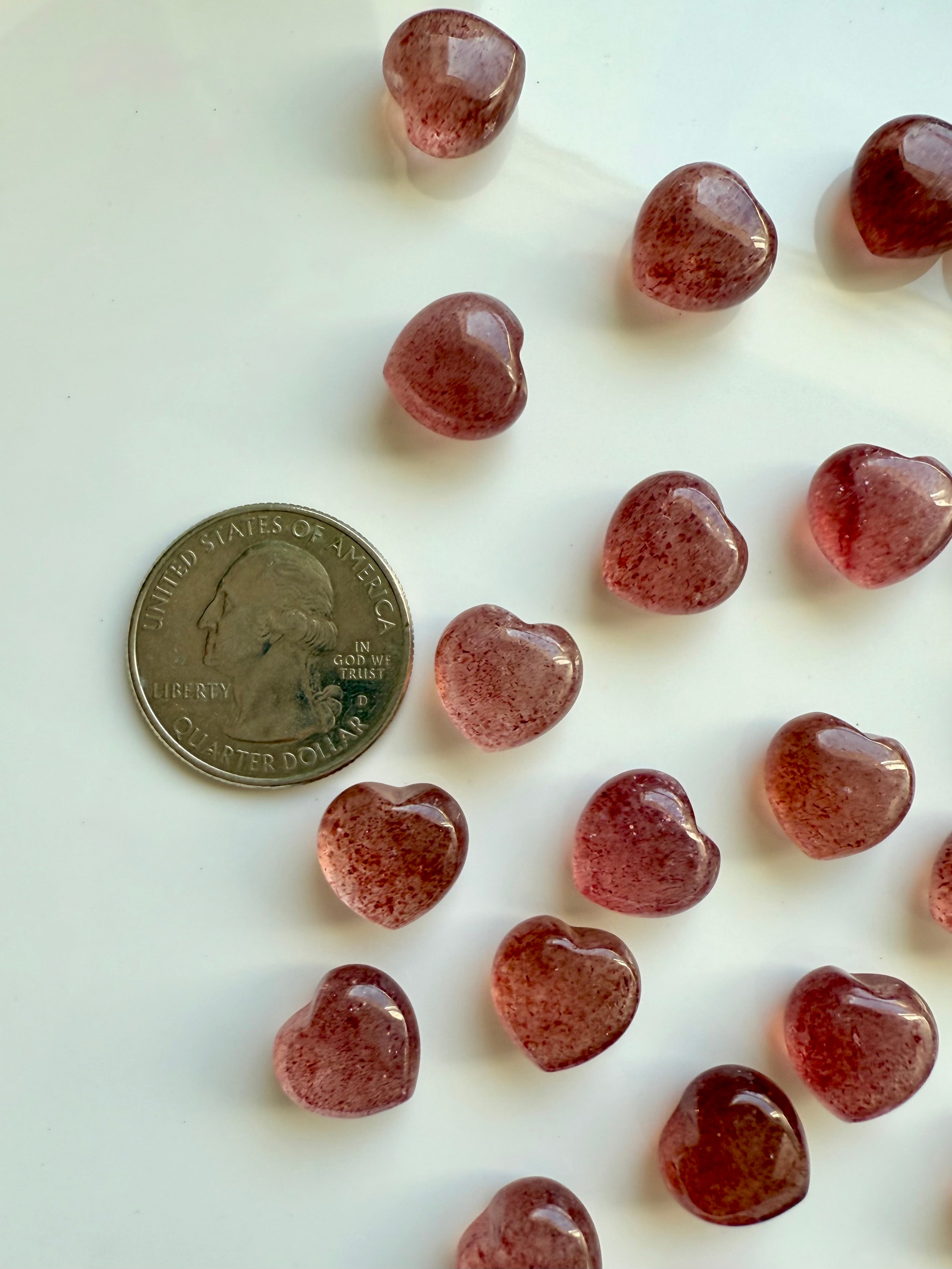 Strawberry Quartz hearts shown next to a quarter for size reference — mini crystal carvings for gifts, grids, and altar decor.