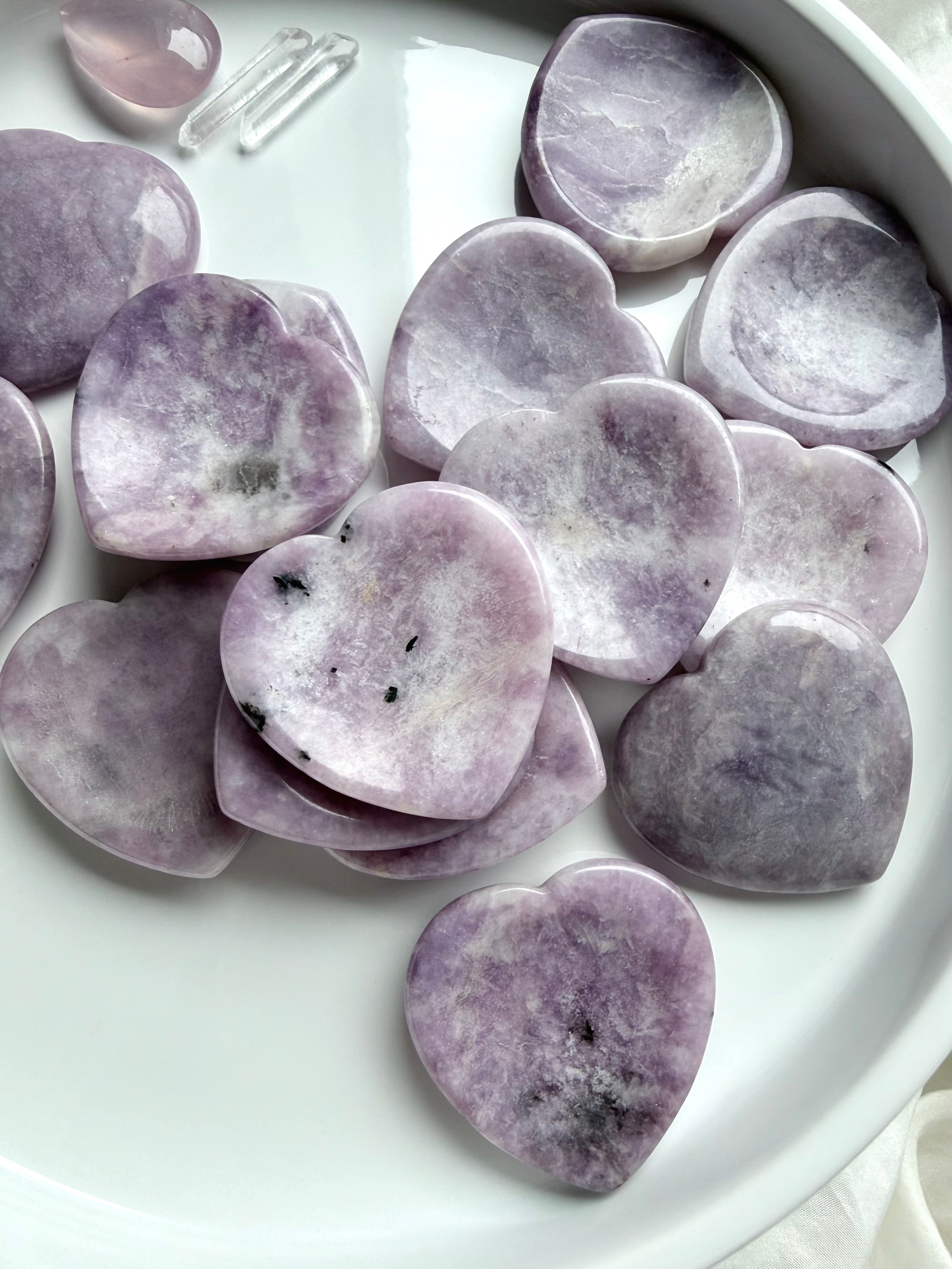 An array of Lepidolite heart thumb stones with lavender purple mottling and natural inclusions