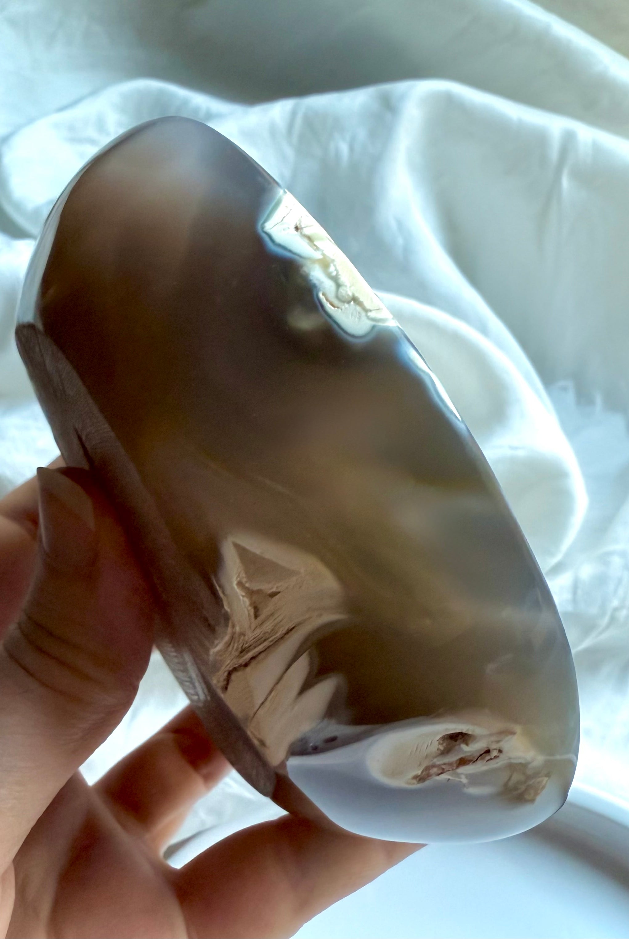 Hand holding polished Orca Agate bowl from a side angle, showing its smooth curved edge and soft grey translucence