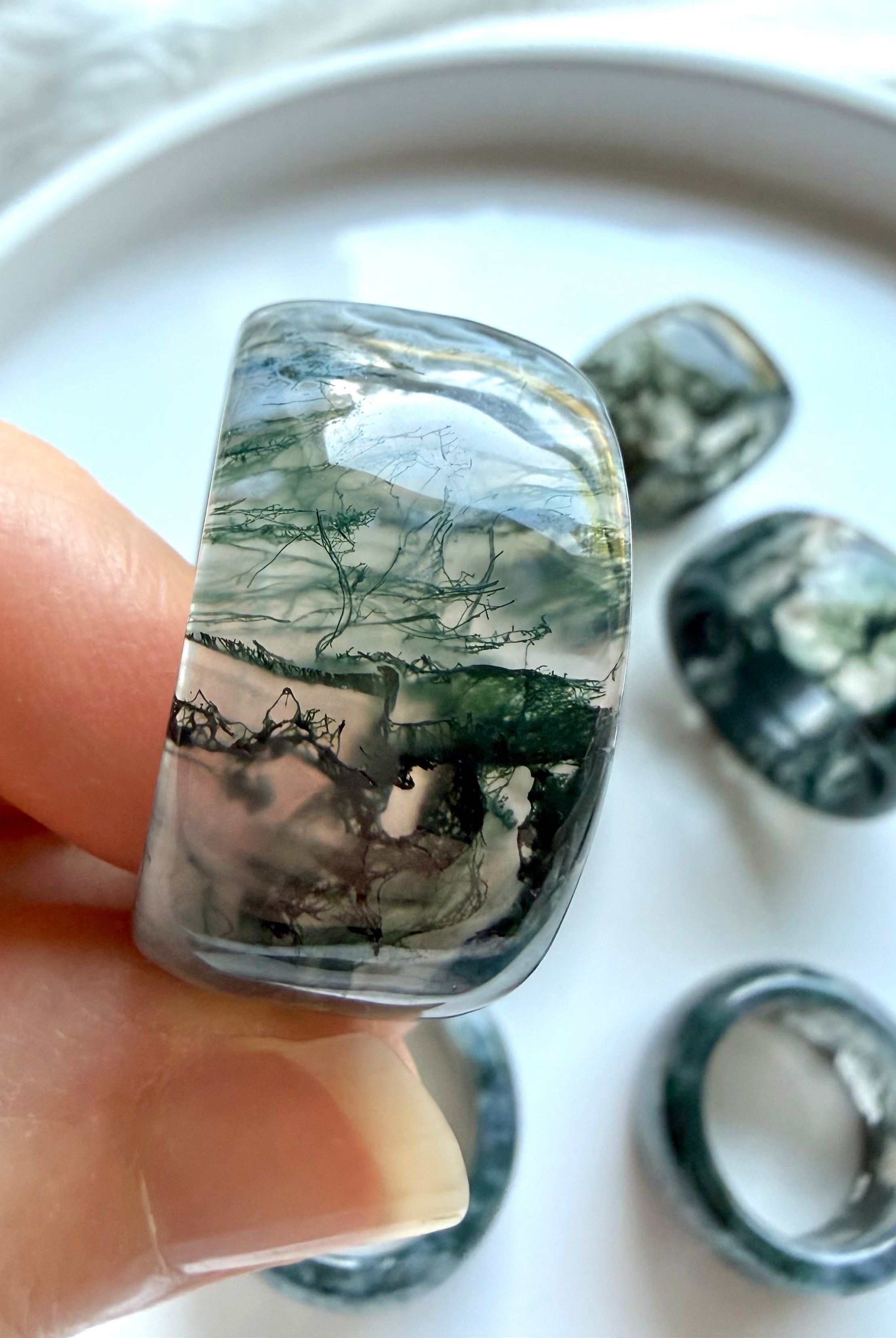 hand holding chunky moss agate wide band ring with natural translucent inclusions and polished glossy finish