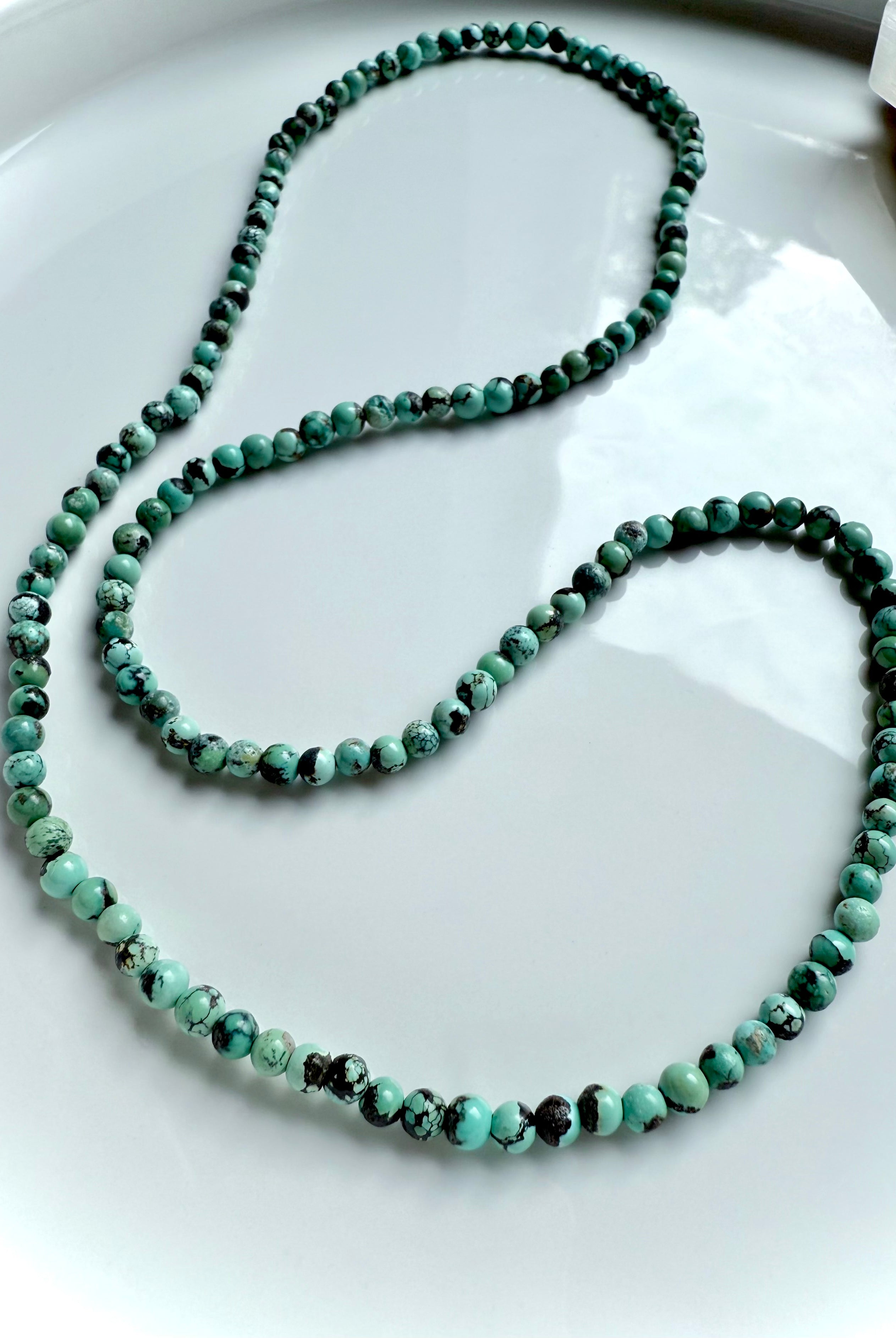 Turquoise necklace variation displayed in an elegant loop with smooth, natural gemstone beads in blue-green tones