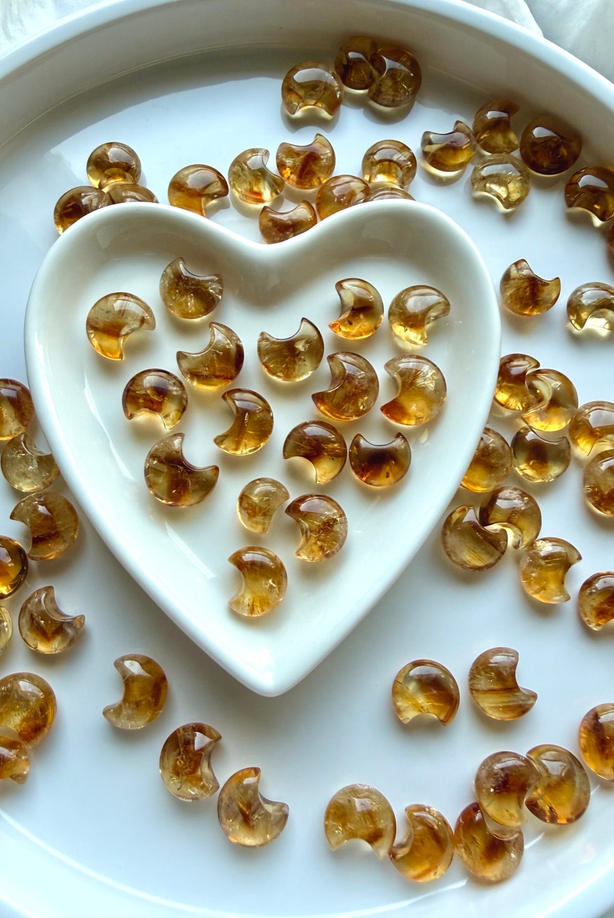Mini Citrine moons arranged around a white heart-shaped dish showing their range of golden honey and amber color