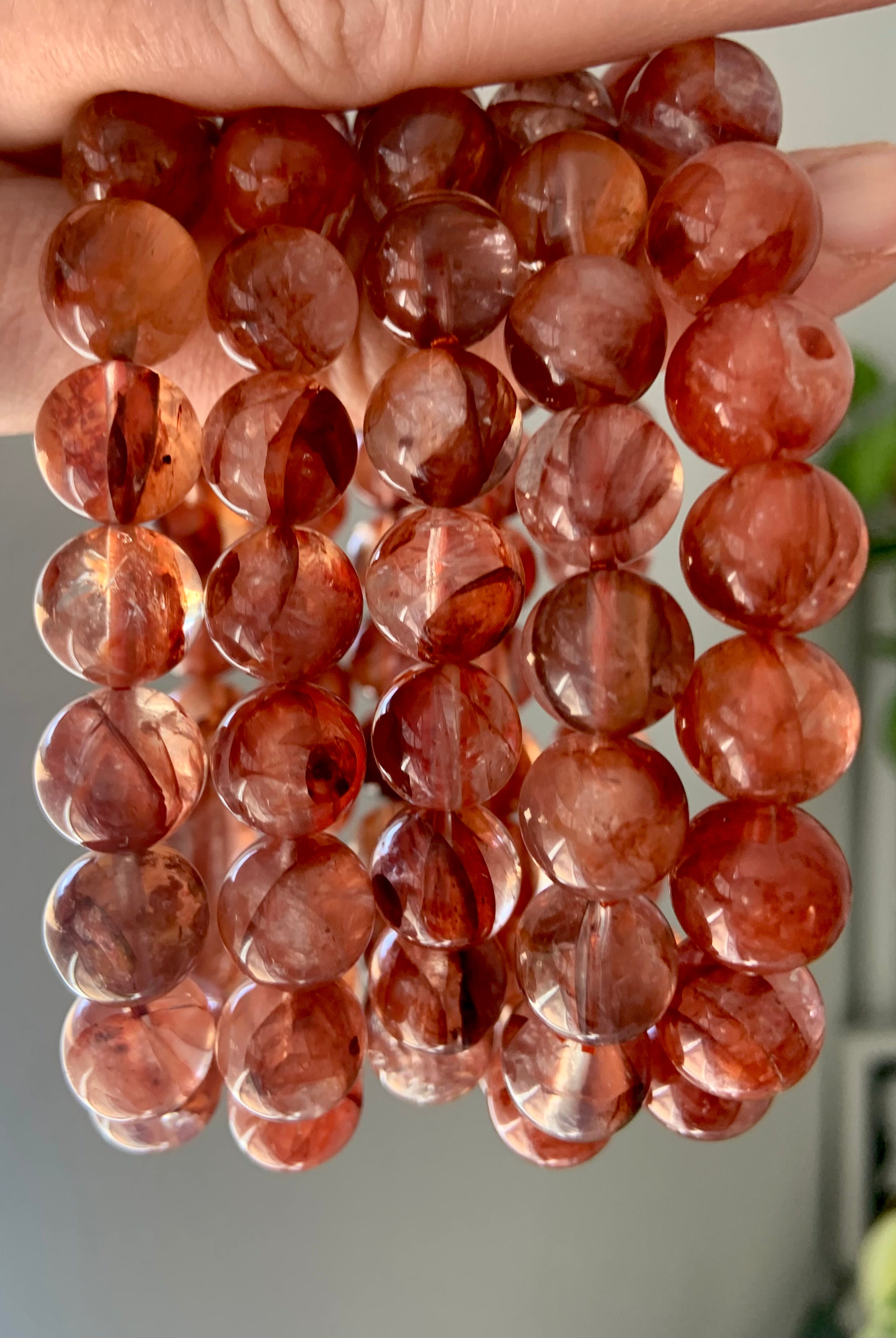 Several Fire Quartz crystal bracelets held to the light, showing red Hematoid Quartz beads in 11.2mm and 11.8mm sizes with natural clarity and color