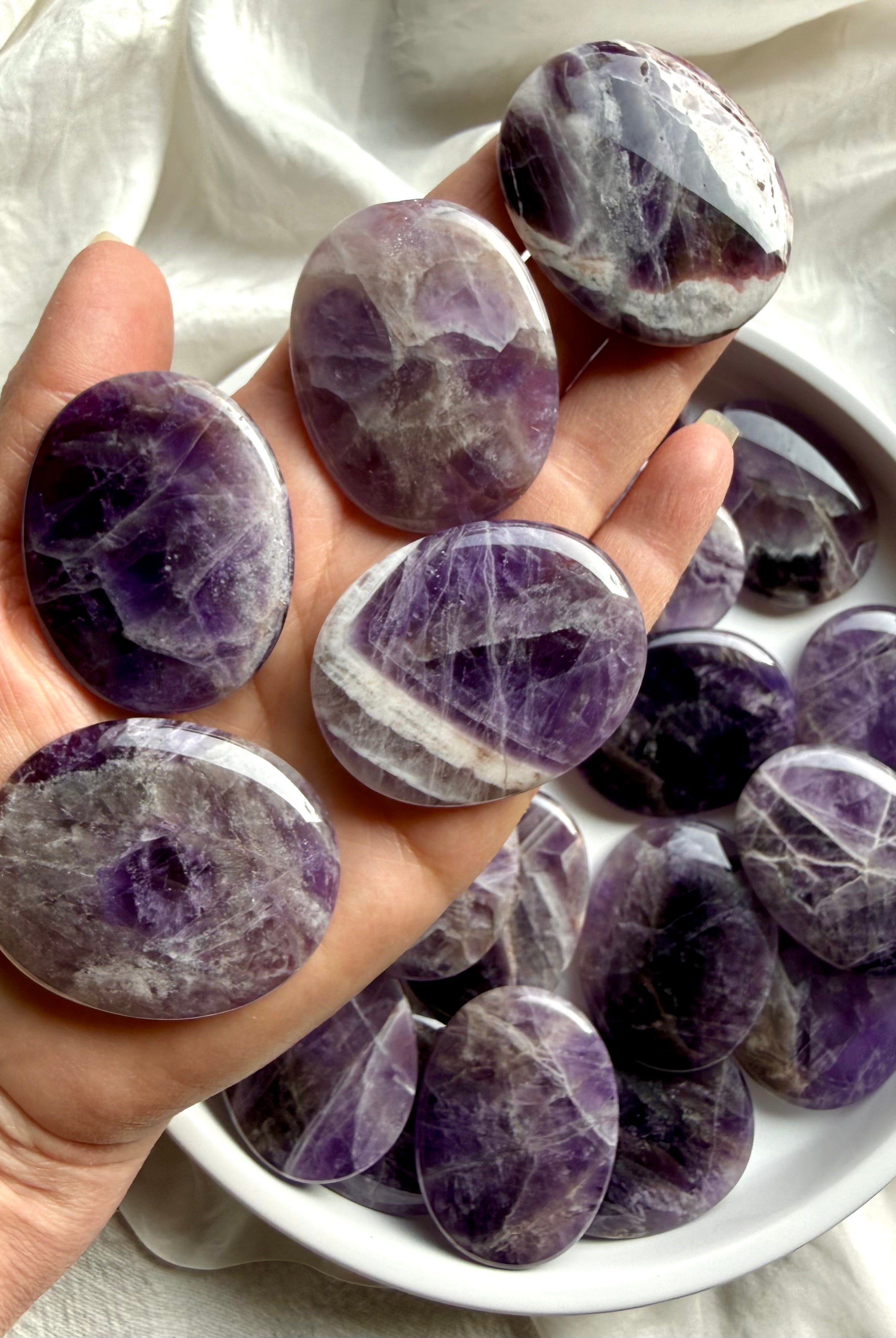 Dream amethyst palm stones shown on hand highlighting slim flat shape, smooth polish, and pocket-friendly thickness