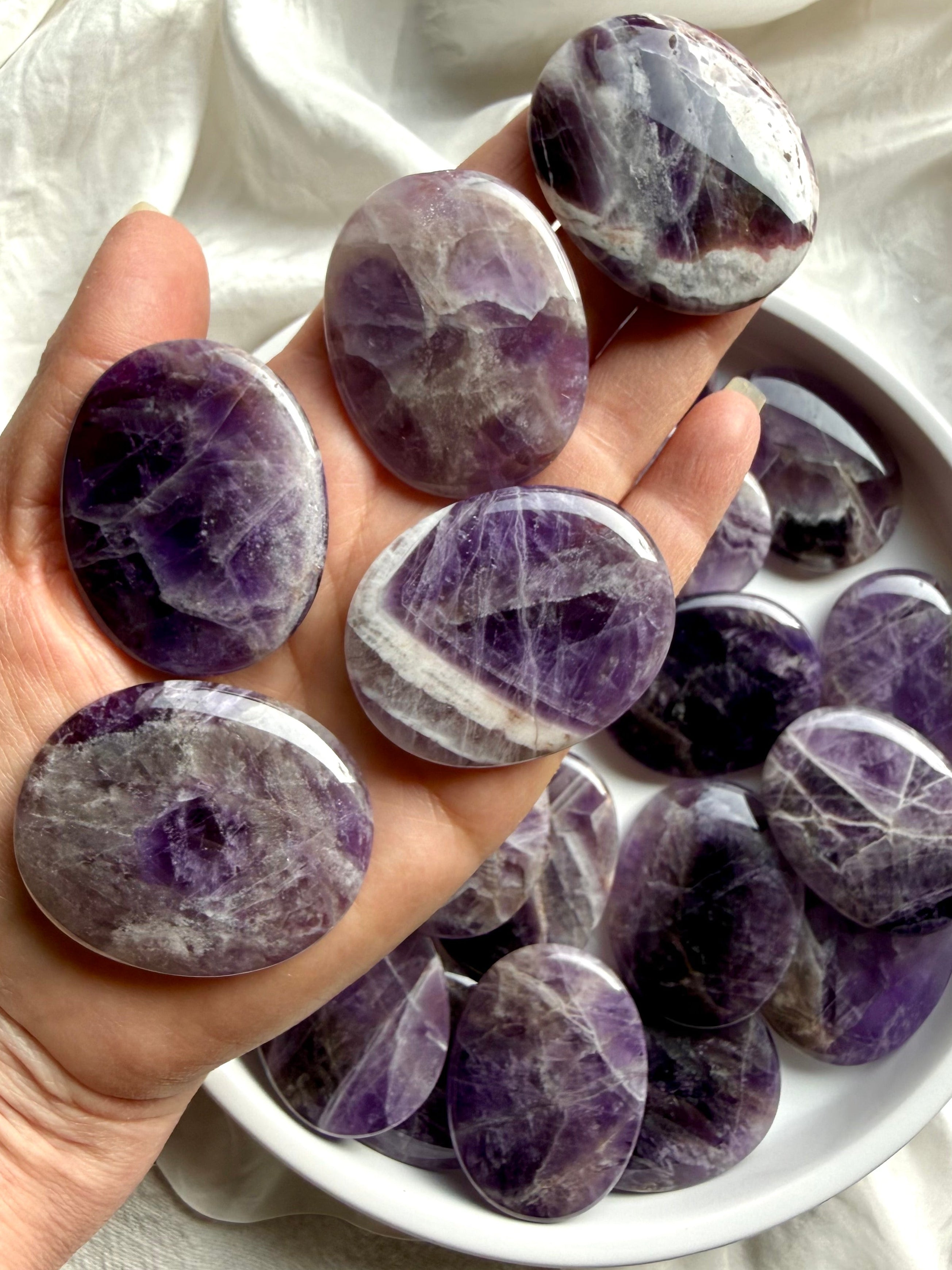 Dream amethyst palm stones shown on hand highlighting slim flat shape, smooth polish, and pocket-friendly thickness