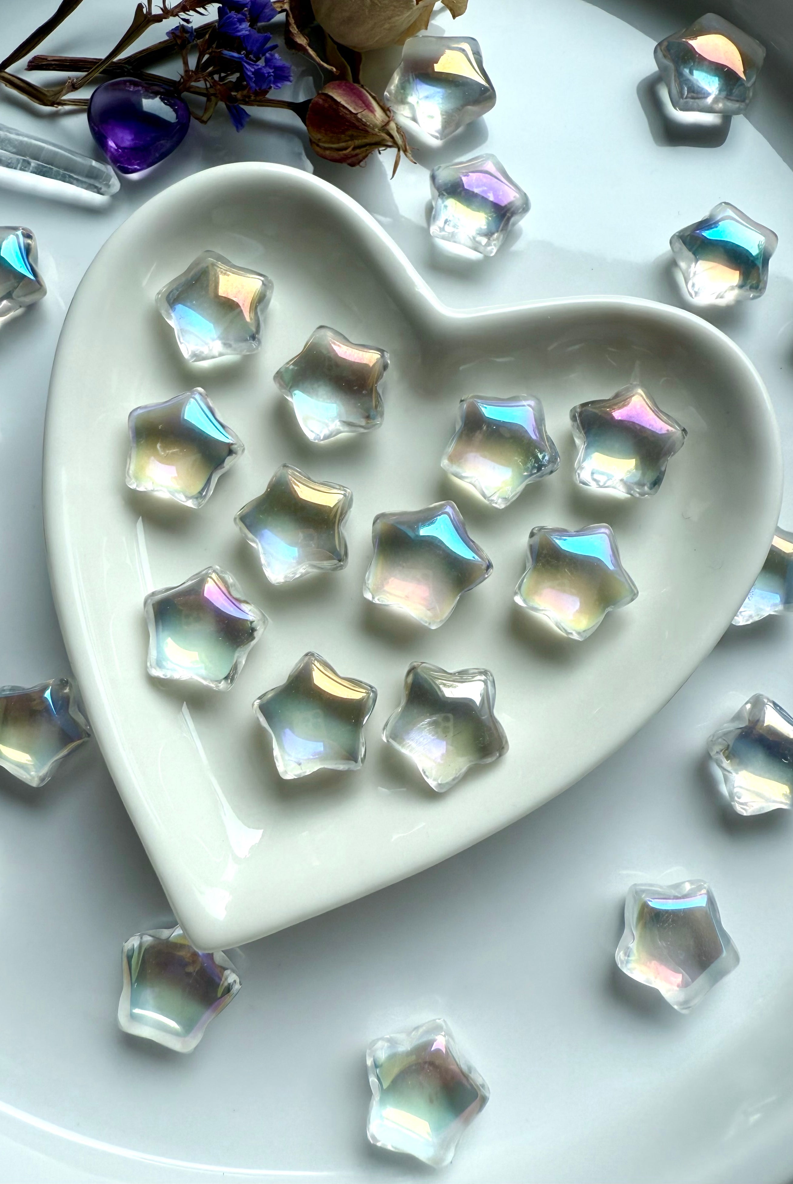 Mini aura quartz stars with rainbow flash displayed in white ceramic heart dish with dried flowers — crystal carvings for chakra healing and décor