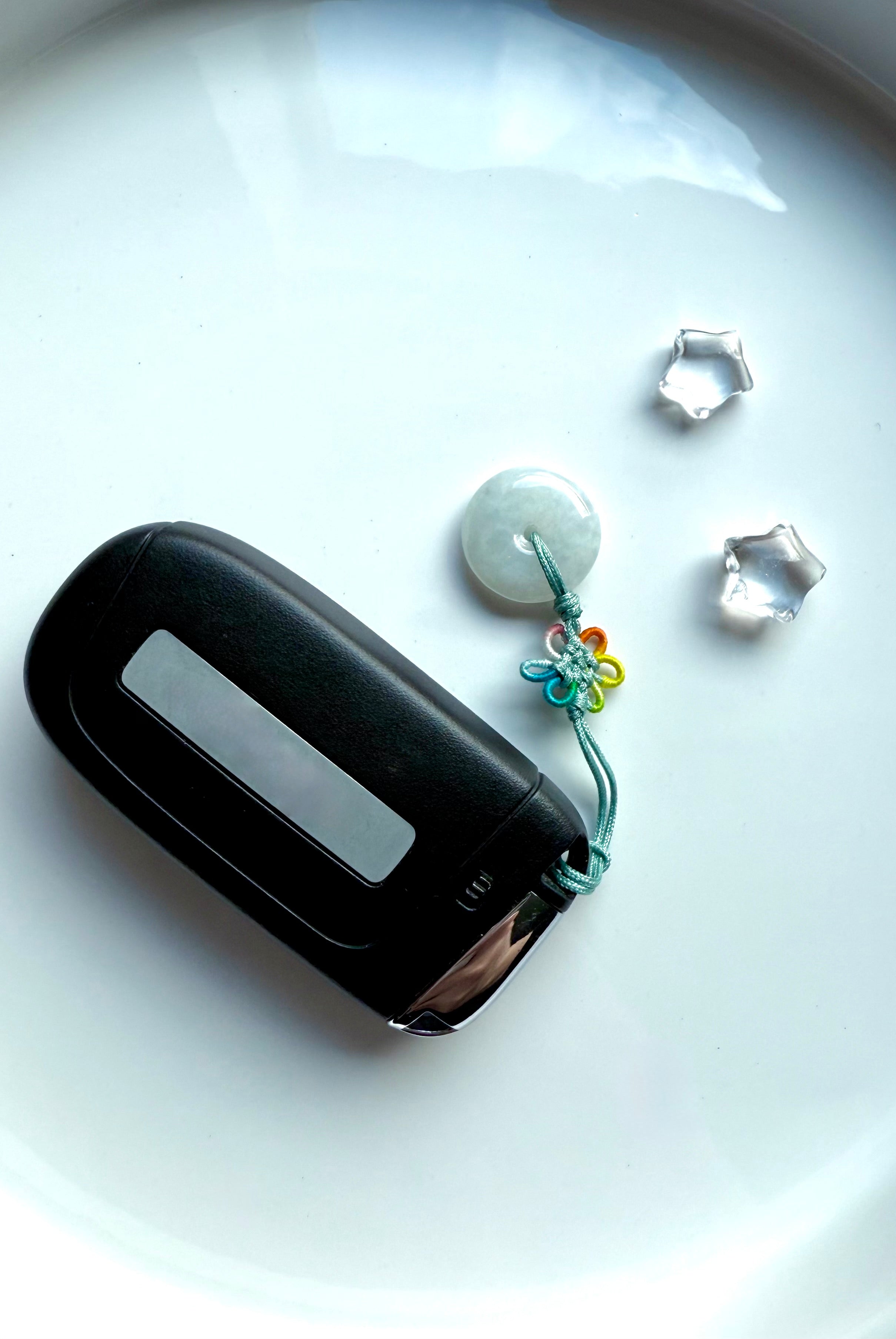 Jade peace buckle charm with rainbow lucky knot used as a car fob keychain, shown on a white ceramic plate