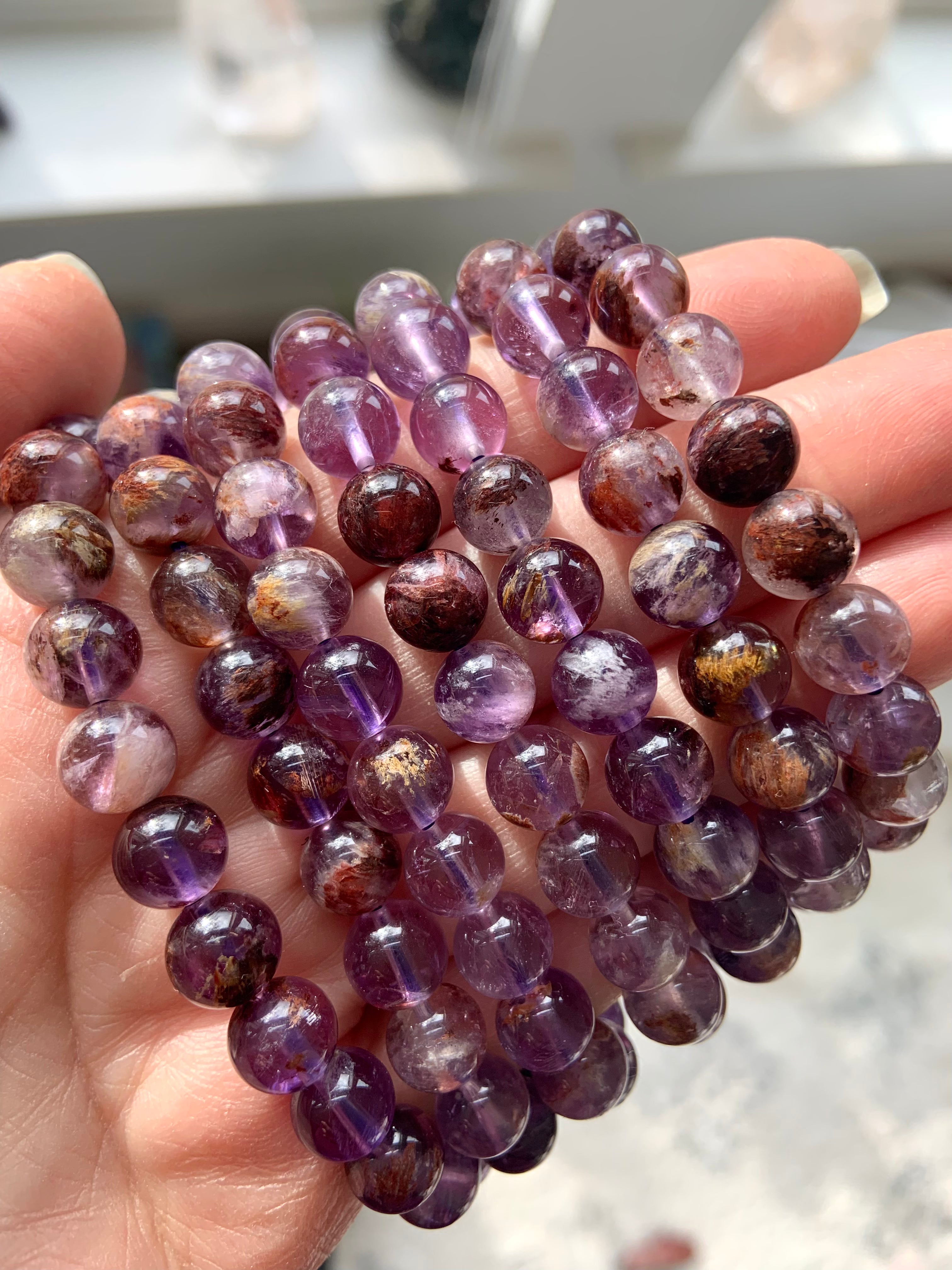 A hand wearing a stackable stretchy bracelet made of natural stones with a purple and multicolored pattern.