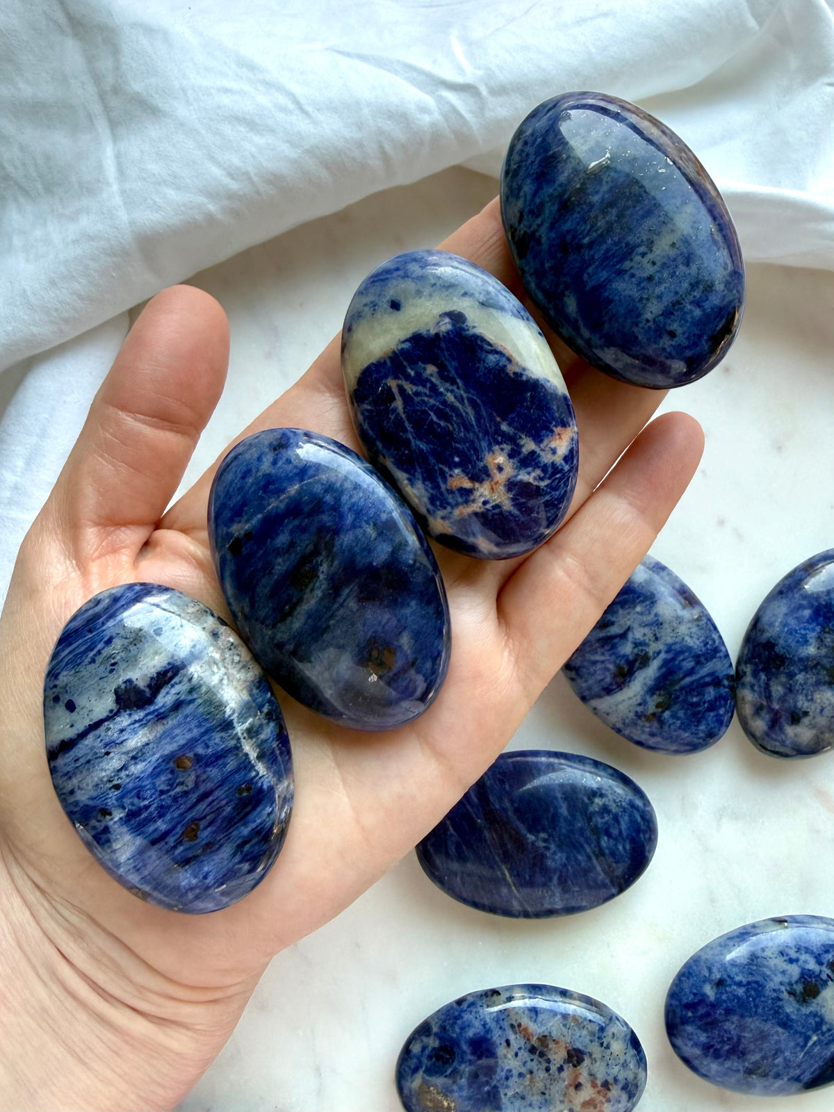 Blue Sodalite palm stones held in hand showing polished oval shape, size, and natural pattern variation